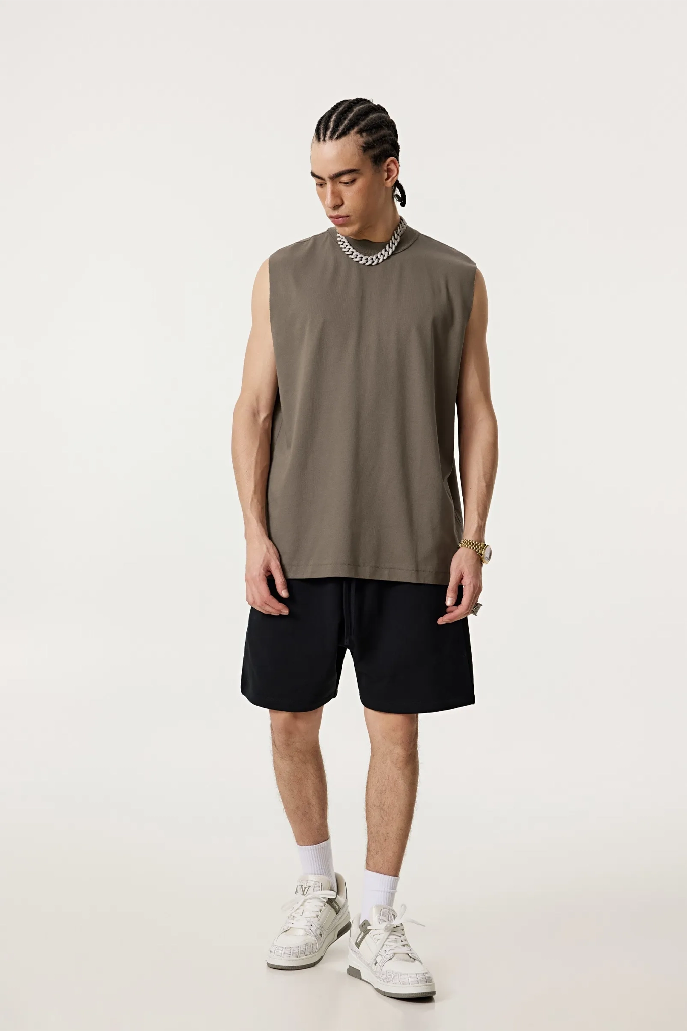 Man wearing a sleeveless brown shirt, black shorts, and white sneakers on a white background