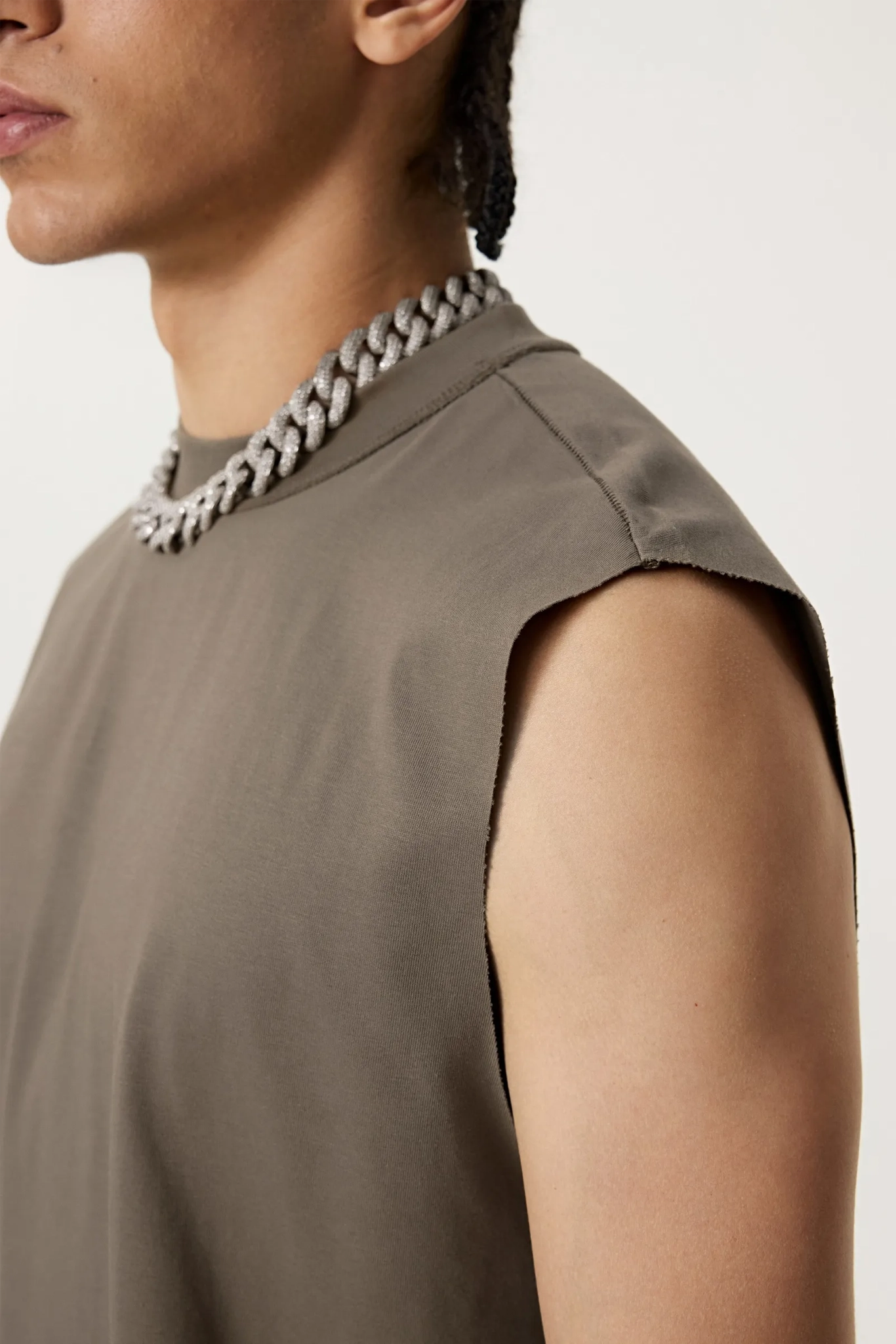 Person wearing a sleeveless top and necklace on a plain background