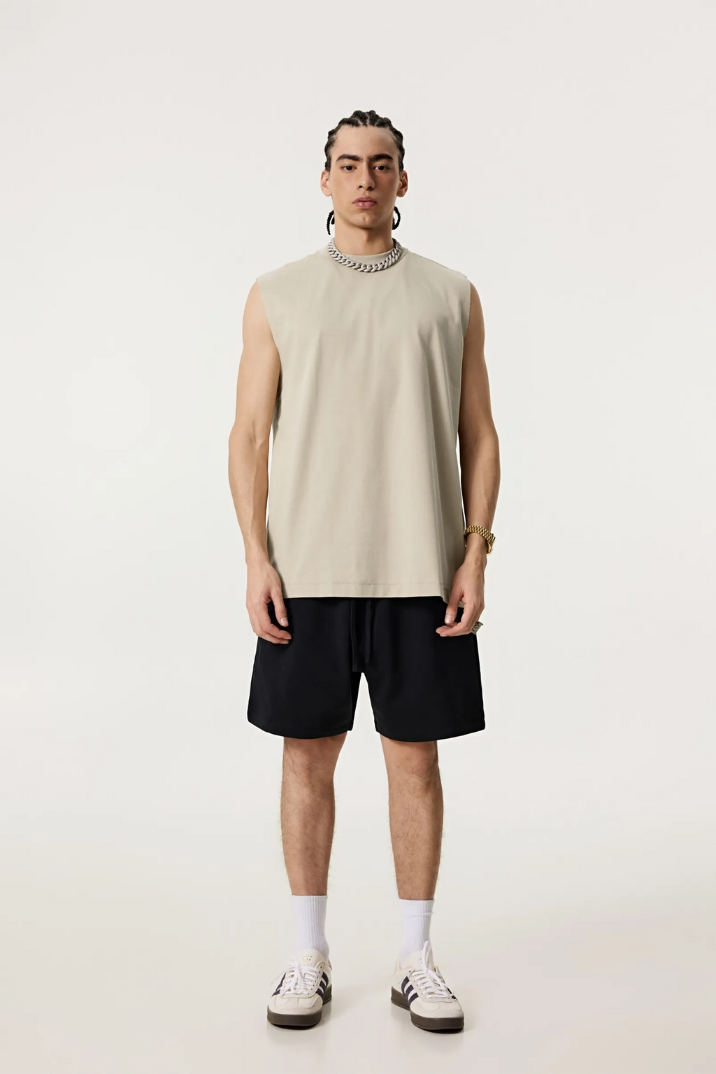 Person wearing a beige sleeveless shirt and black shorts on a white background