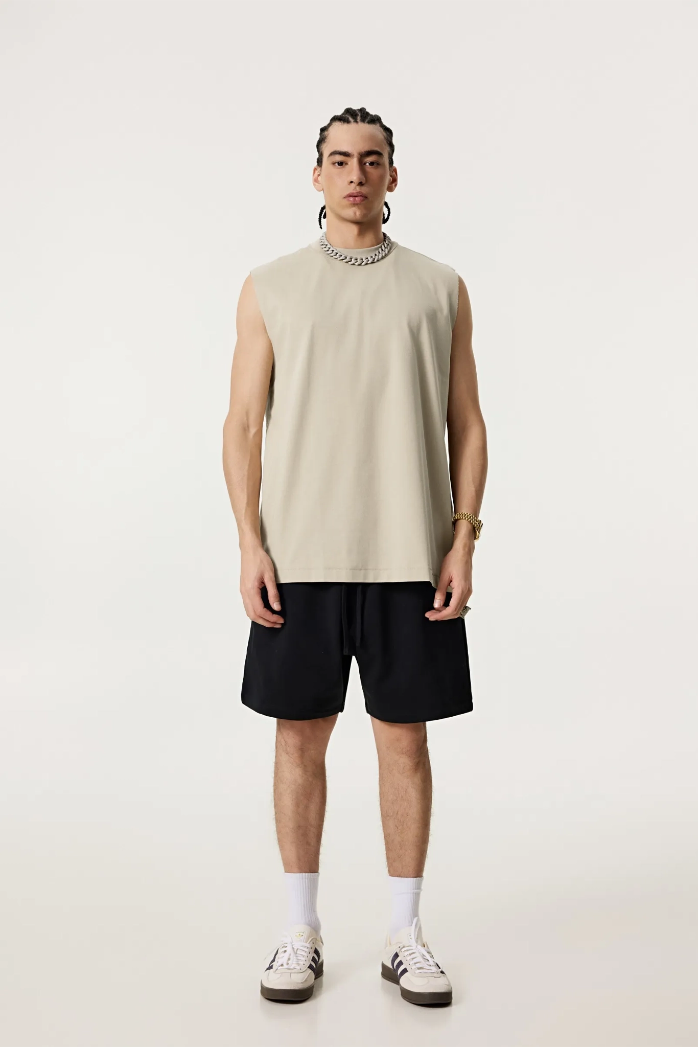 Person wearing a beige sleeveless shirt and black shorts on a white background