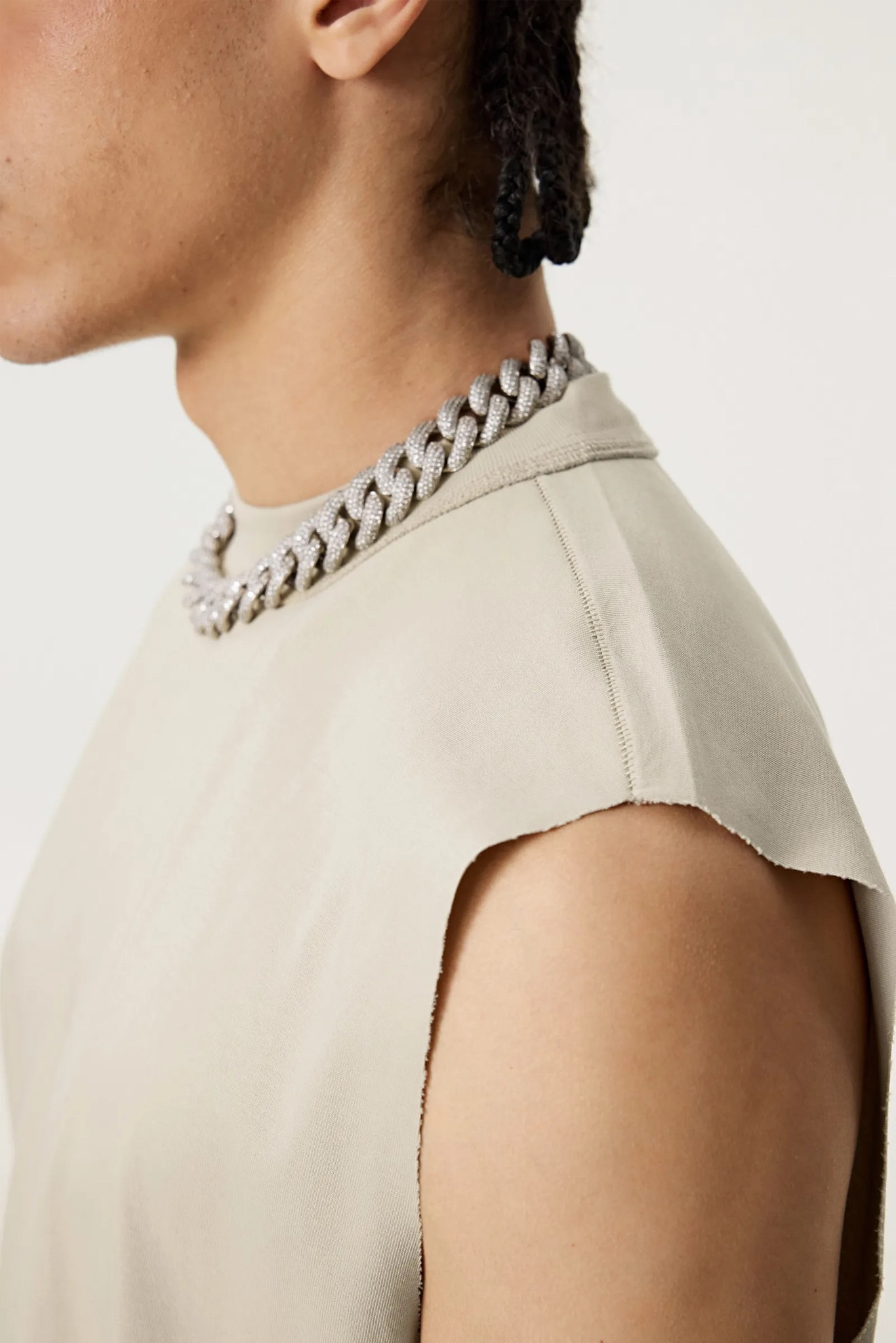 Close-up of a person wearing a beige top with a chain detail on a plain background