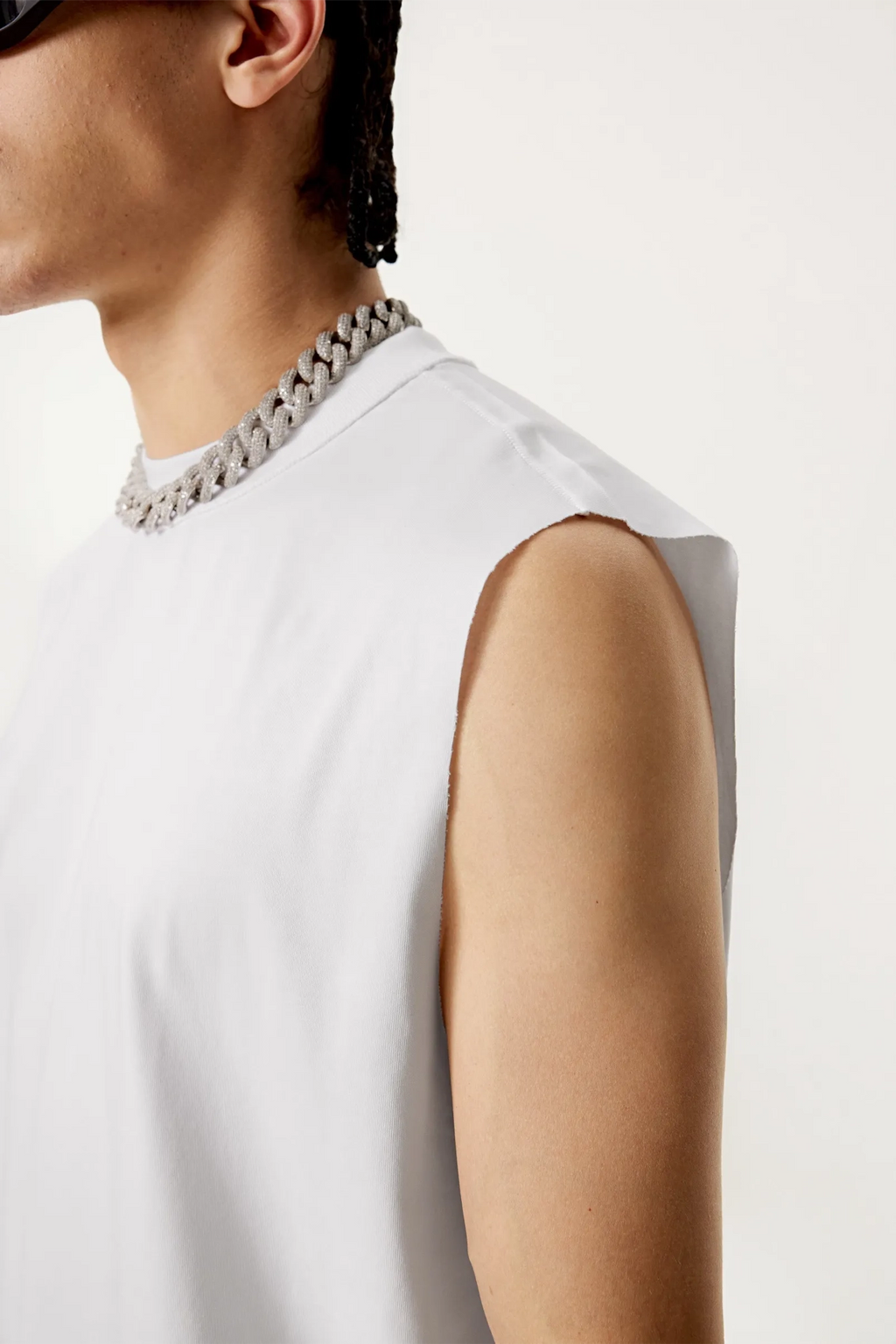 Person wearing a white sleeveless top with a chain necklace on a plain background