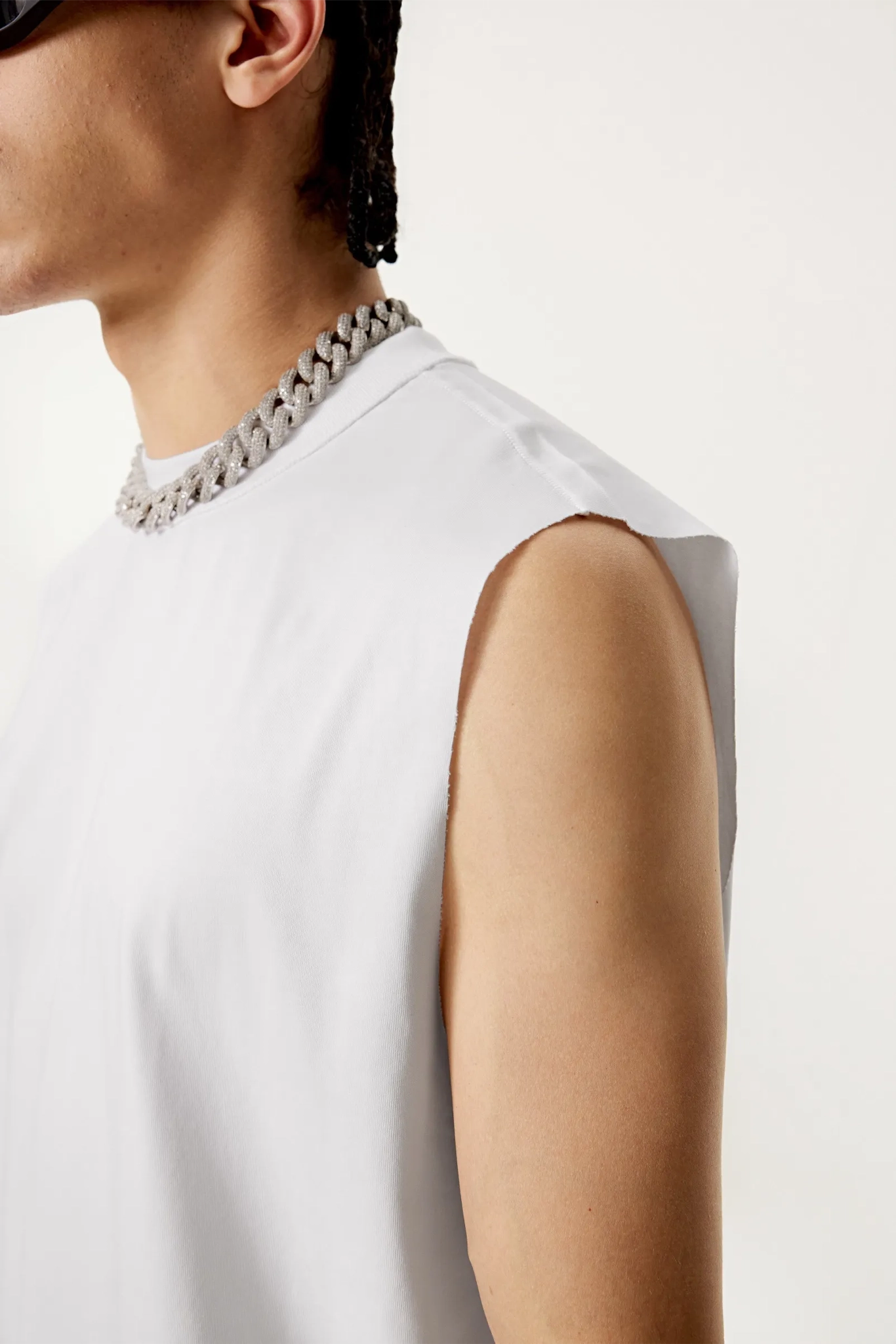 Person wearing a white sleeveless top with a chain necklace on a plain background