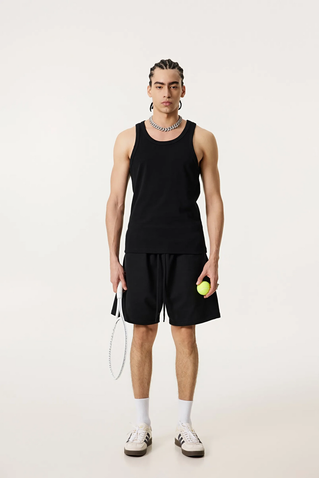 Person wearing a black tank top and shorts holding a tennis ball on a white background