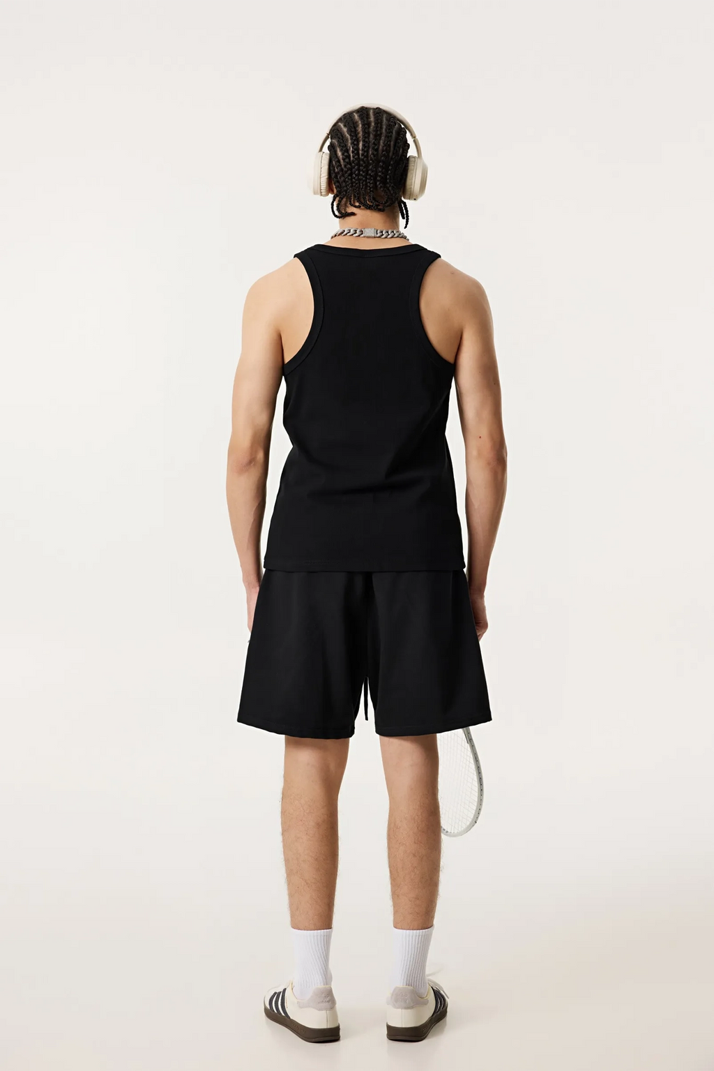 Person wearing a black tank top and shorts with white headphones on a white background