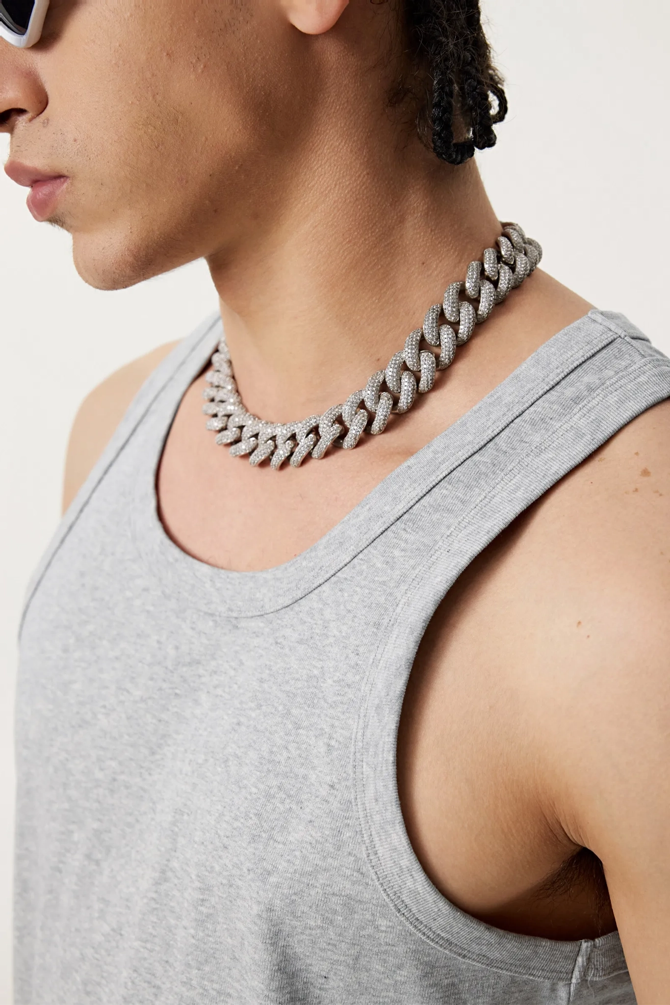 Person wearing a gray tank top and chunky chain necklace on a white background