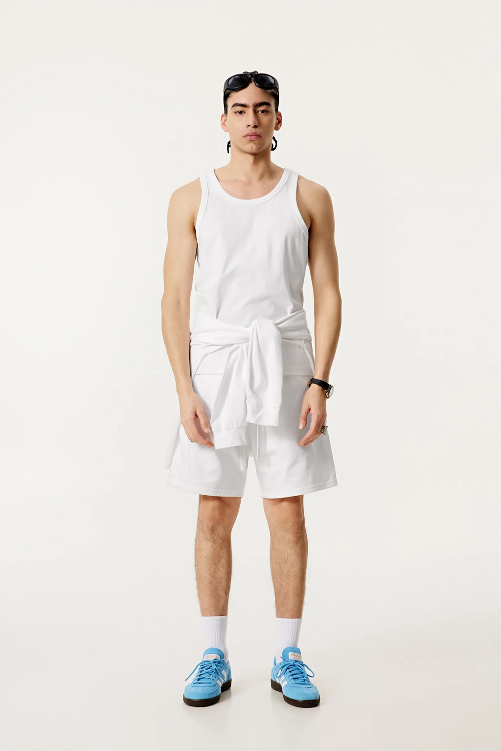 Person wearing a white tank top and shorts with blue sneakers on a white background