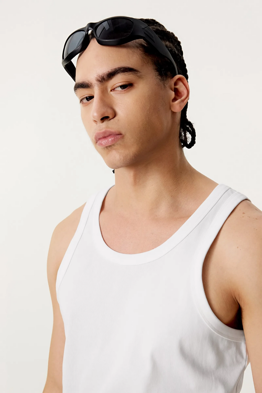 Man wearing a white tank top and black sunglasses on his head against a plain background