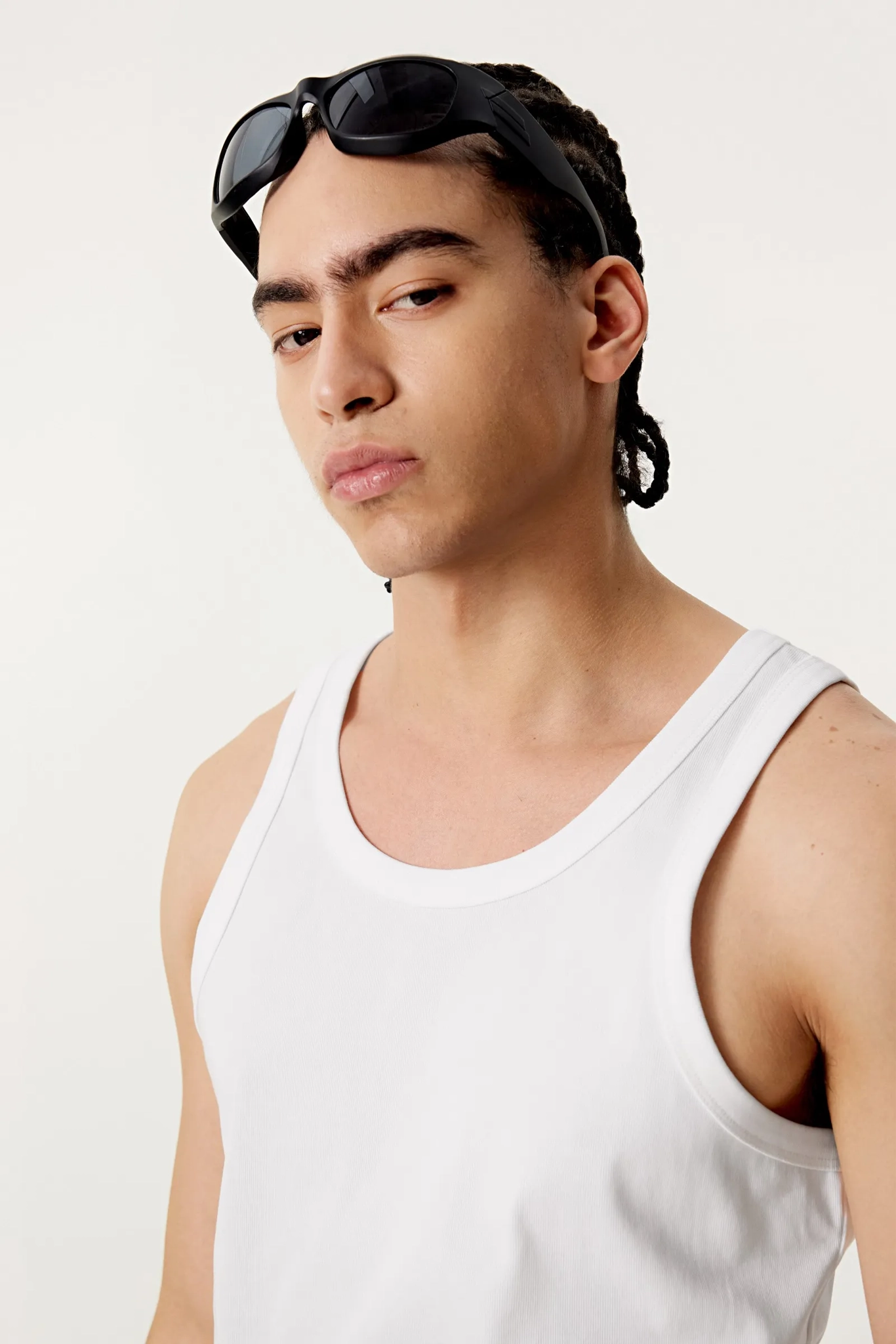 Man wearing a white tank top and black sunglasses on his head against a plain background