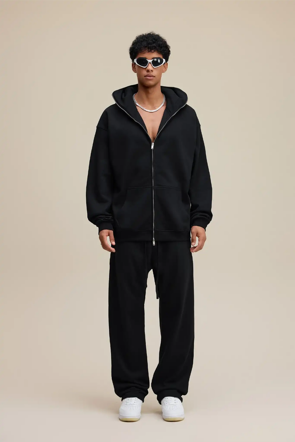 Person wearing a black hoodie and pants with white sneakers on a beige background