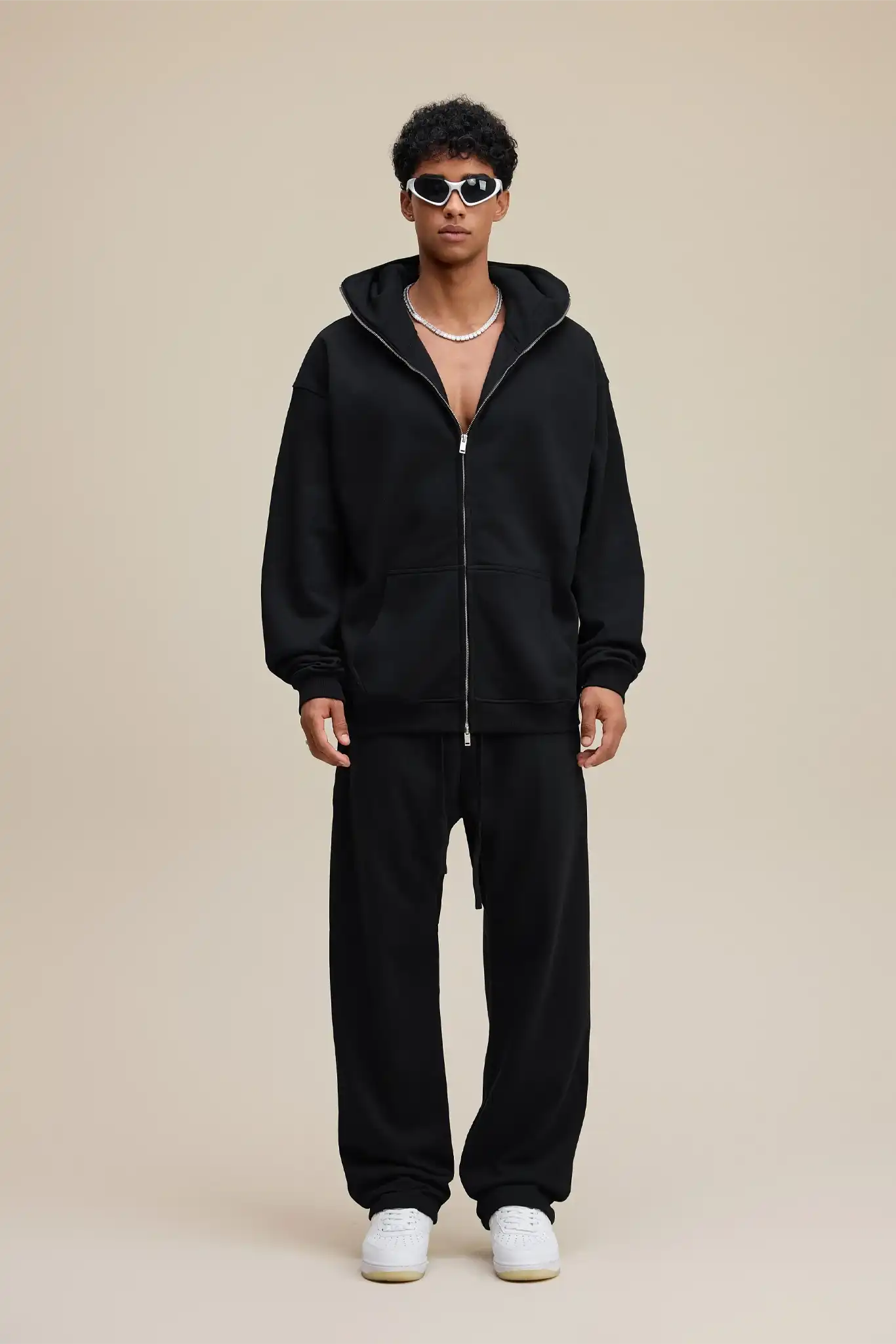 Person wearing a black hoodie and pants with white sneakers on a beige background