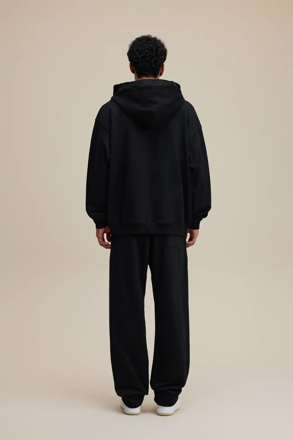 Person wearing a black hoodie and pants on a beige background
