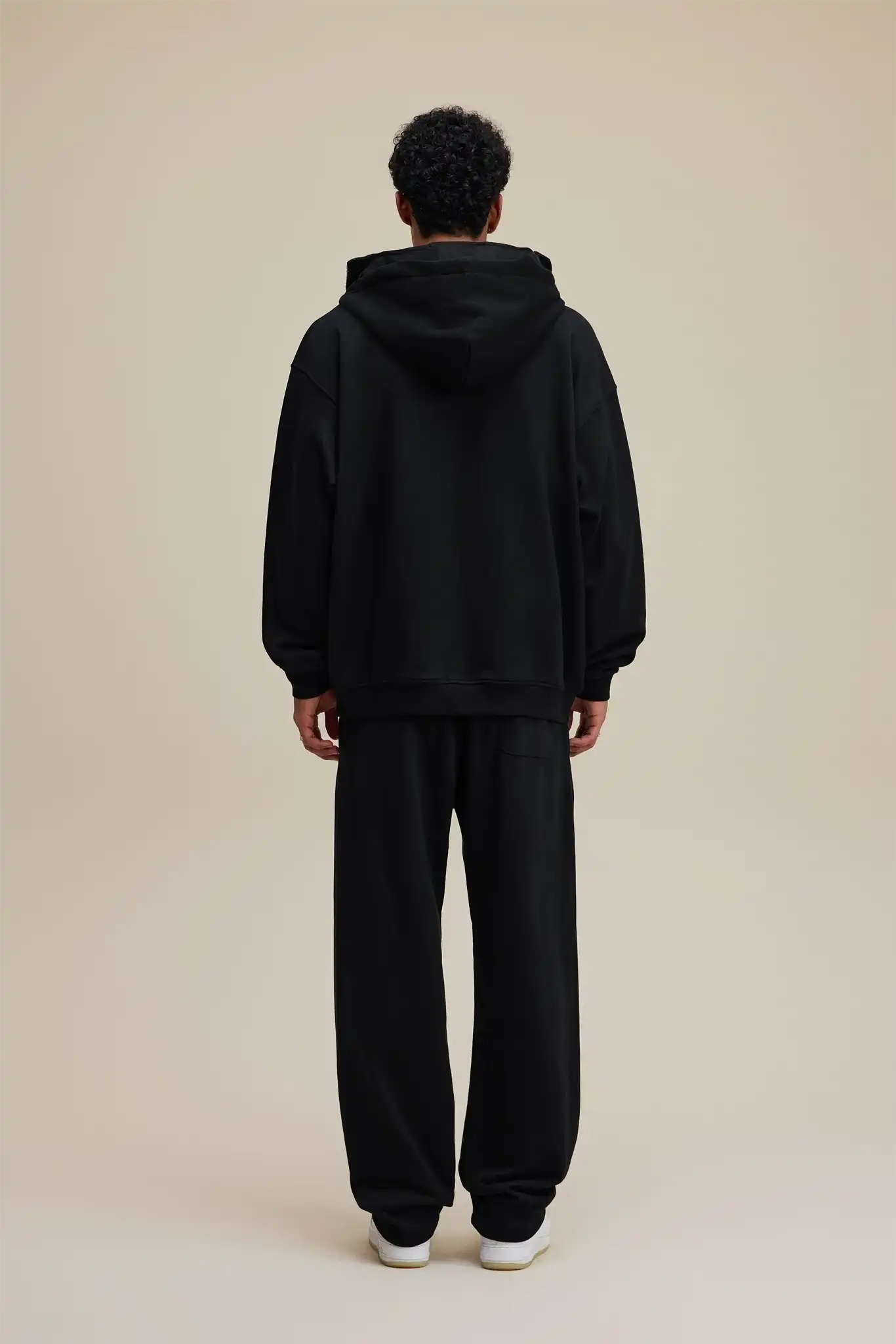 Person wearing a black hoodie and pants on a beige background