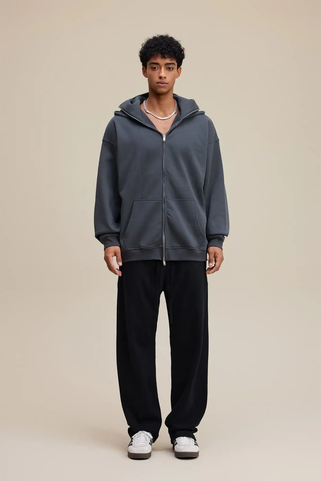 Person wearing a gray hoodie and black pants on a beige background