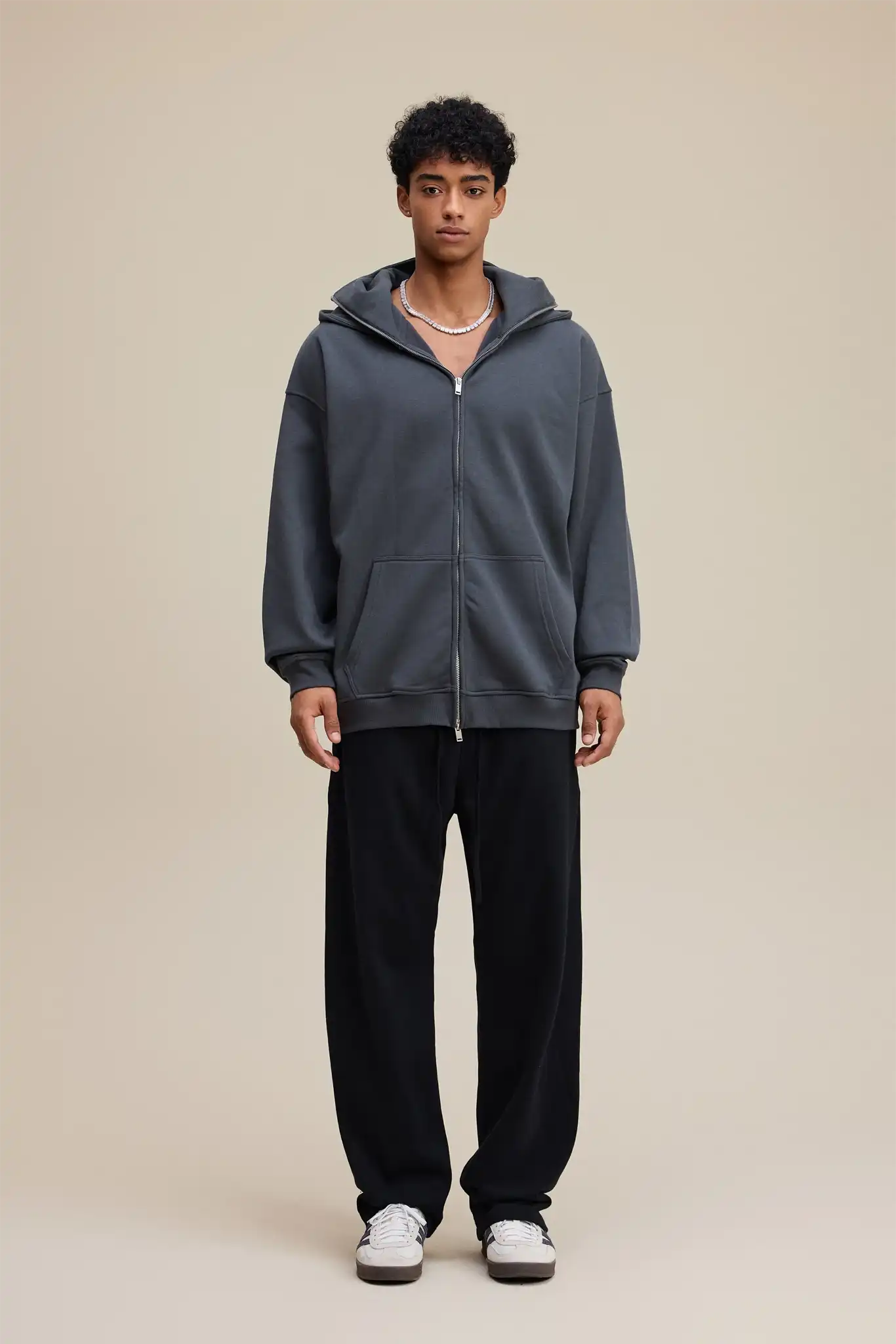 Person wearing a gray hoodie and black pants on a beige background