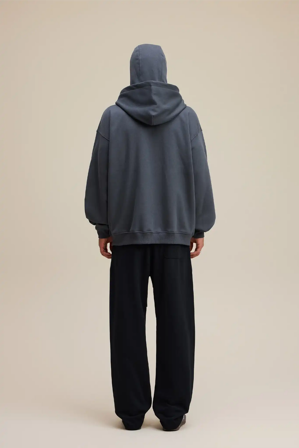 Person wearing a gray hoodie and black pants on a beige background