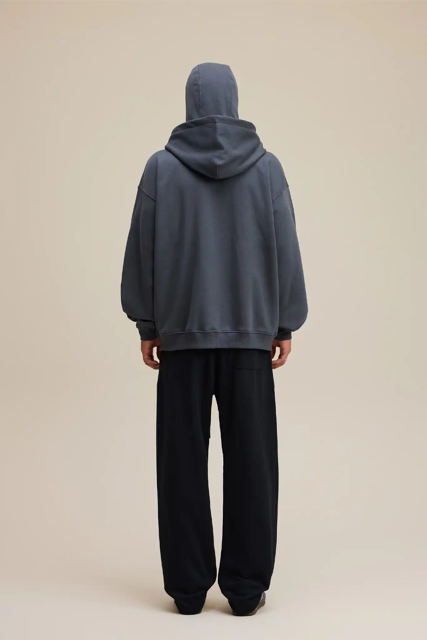 Person wearing a gray hoodie and black pants on a beige background