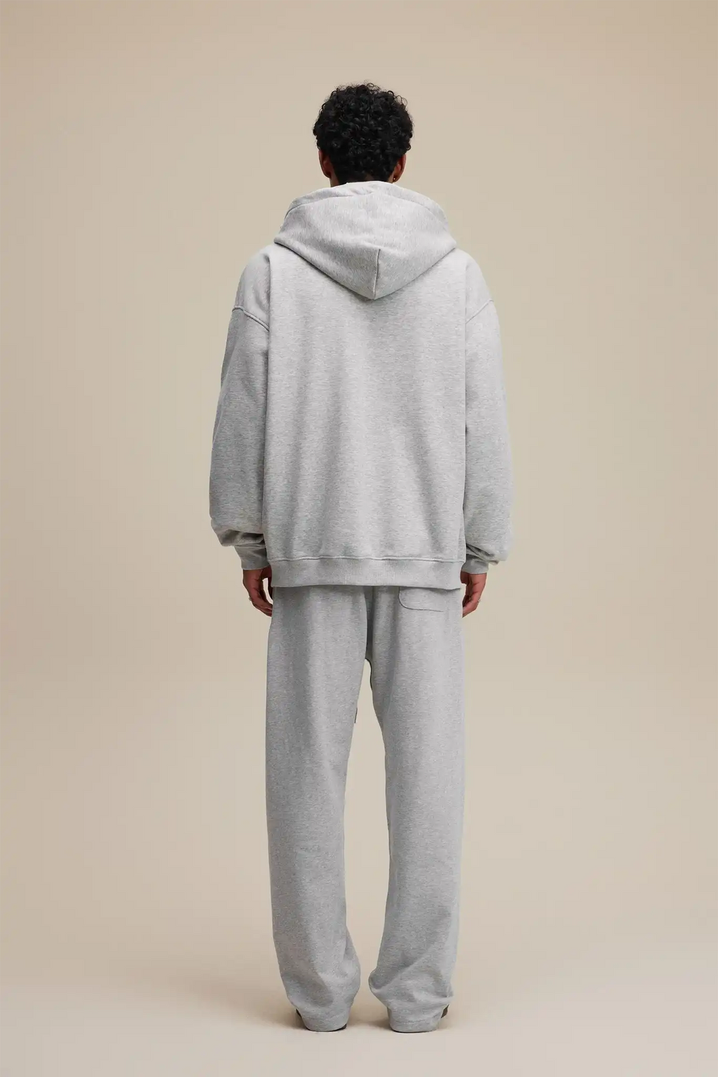 Person wearing a gray hoodie and pants set on a beige background