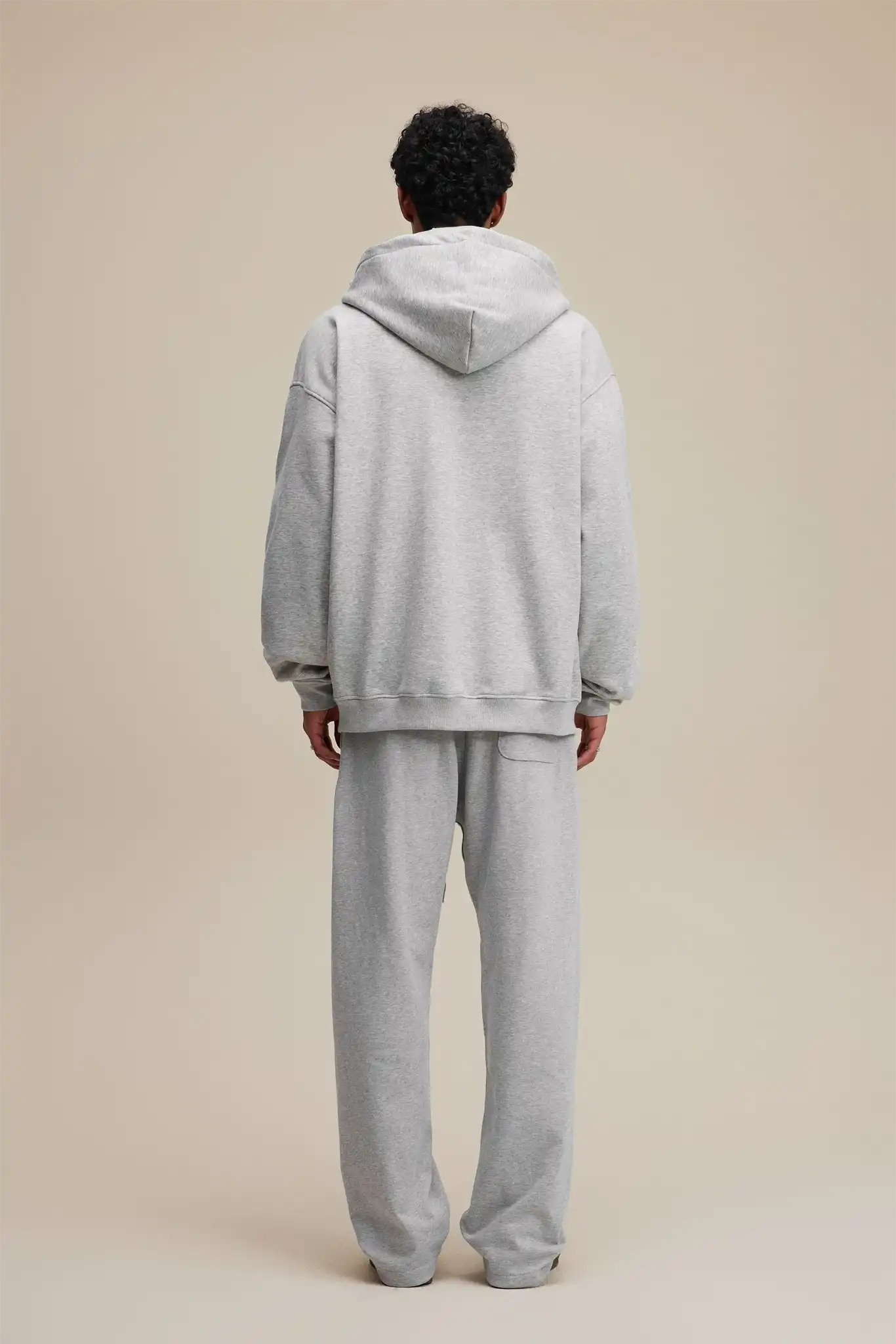 Person wearing a gray hoodie and pants set on a beige background