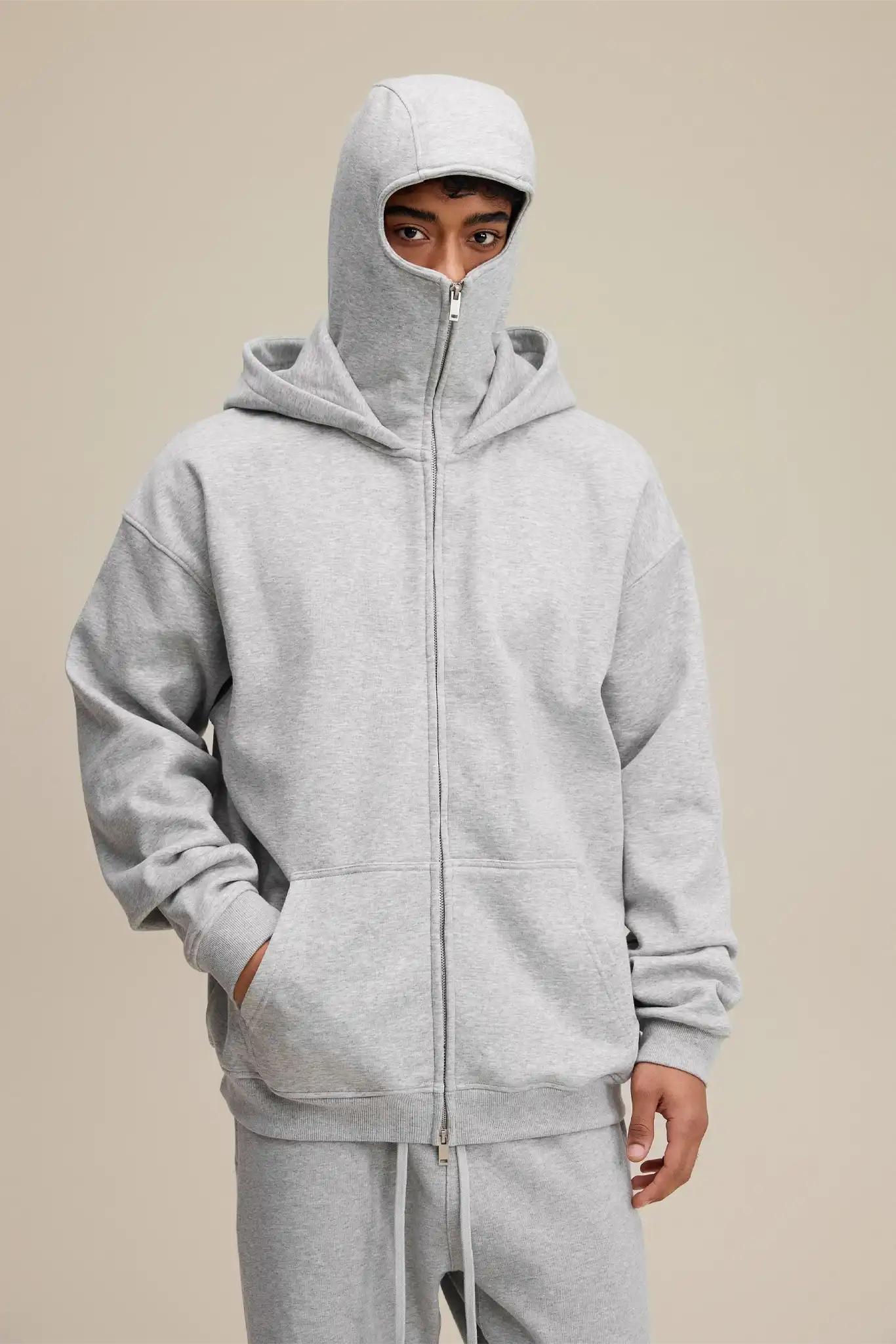 Person wearing a gray hoodie and pants on a beige background