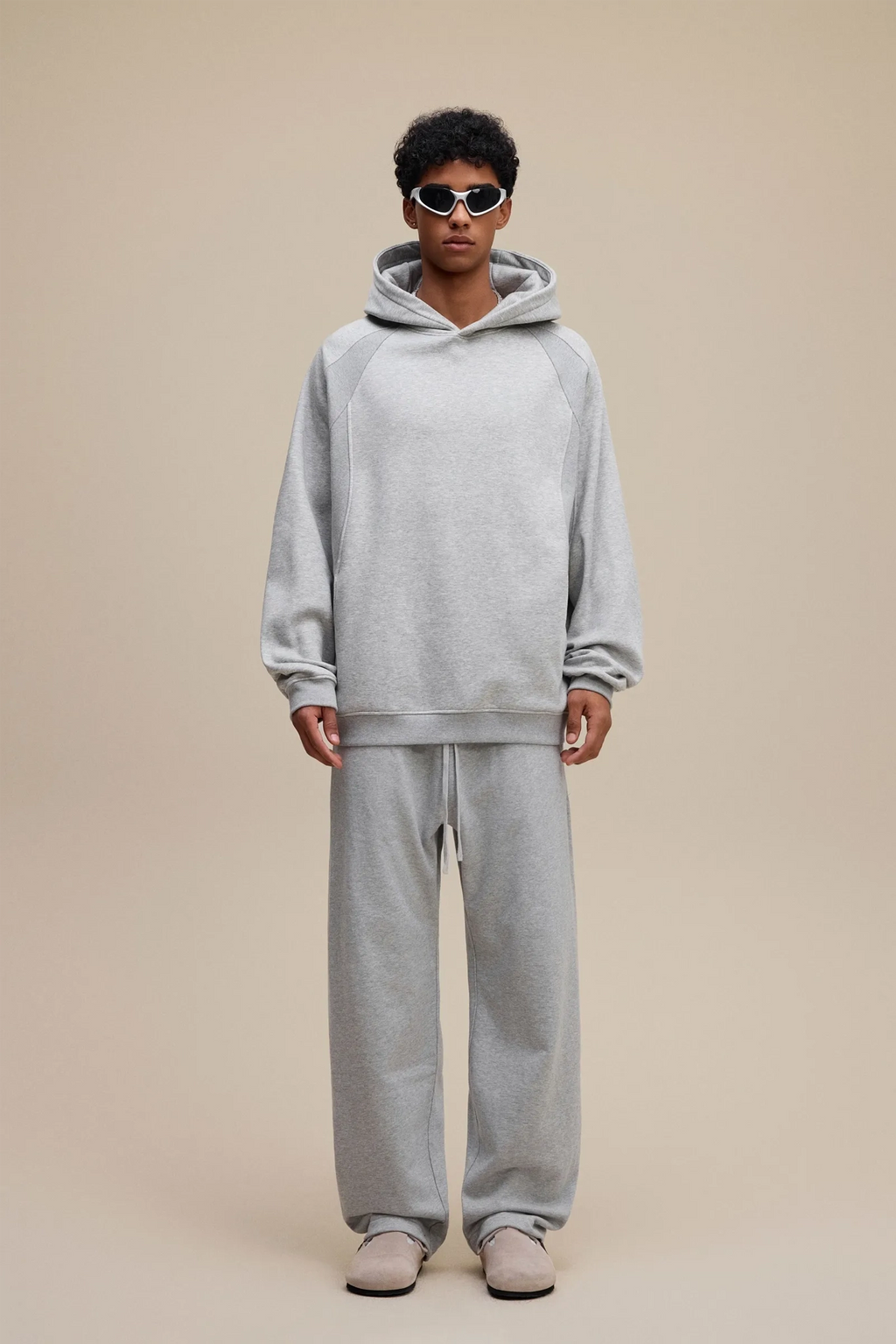 Person wearing a gray hoodie and pants set on a beige background