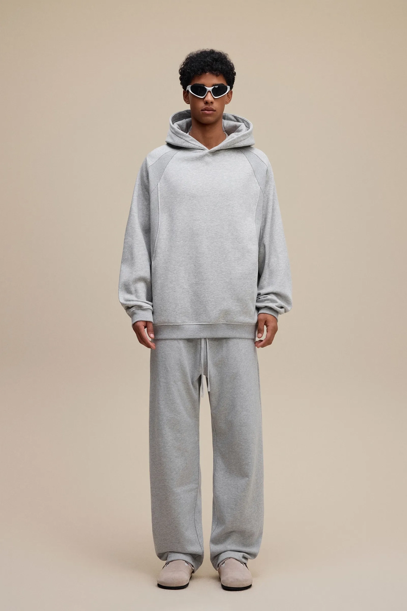 Person wearing a gray hoodie and pants set on a beige background