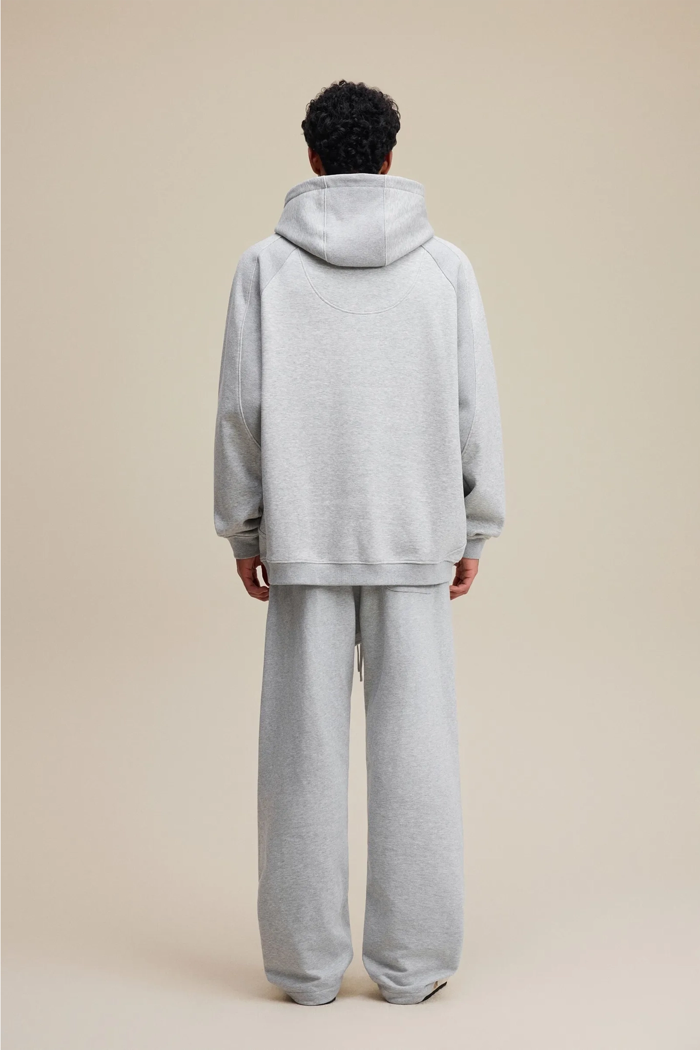 Person wearing a gray hoodie and pants on a beige background