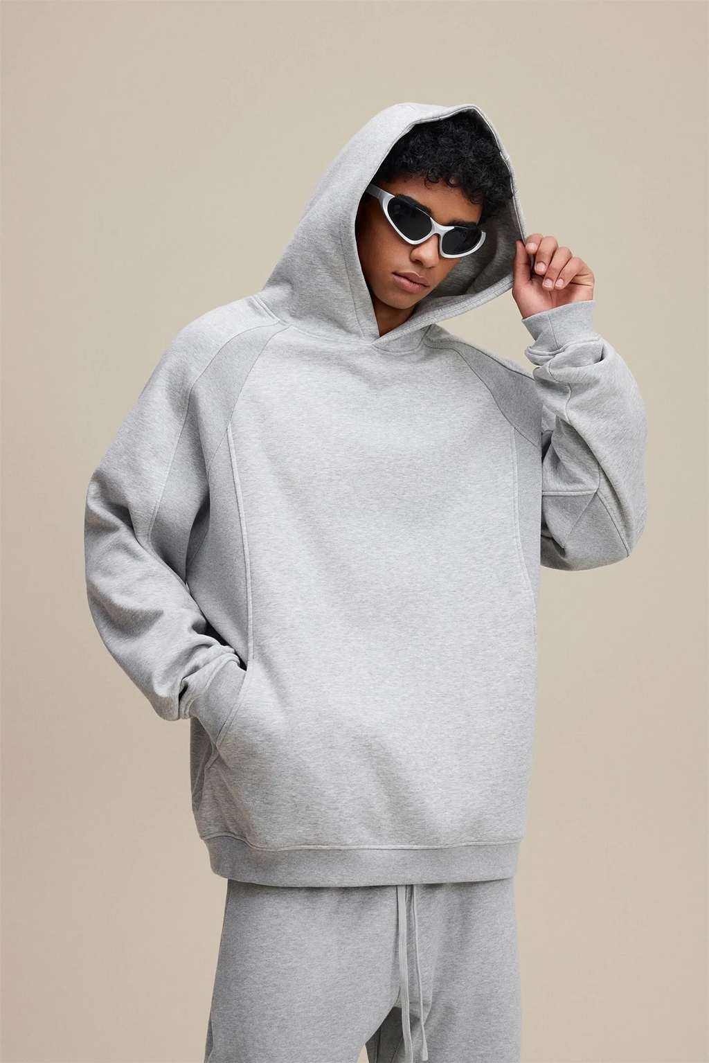 Person wearing a gray hoodie and matching pants on a beige background