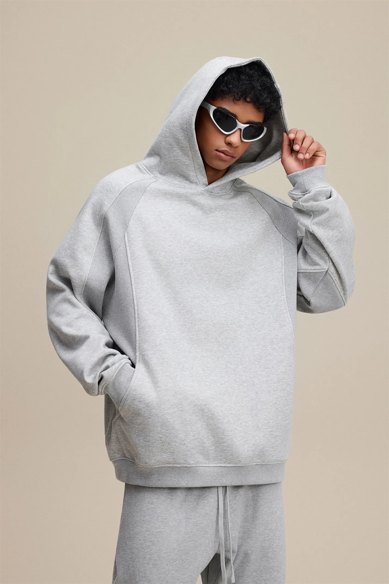 Person wearing a gray hoodie and matching pants on a beige background
