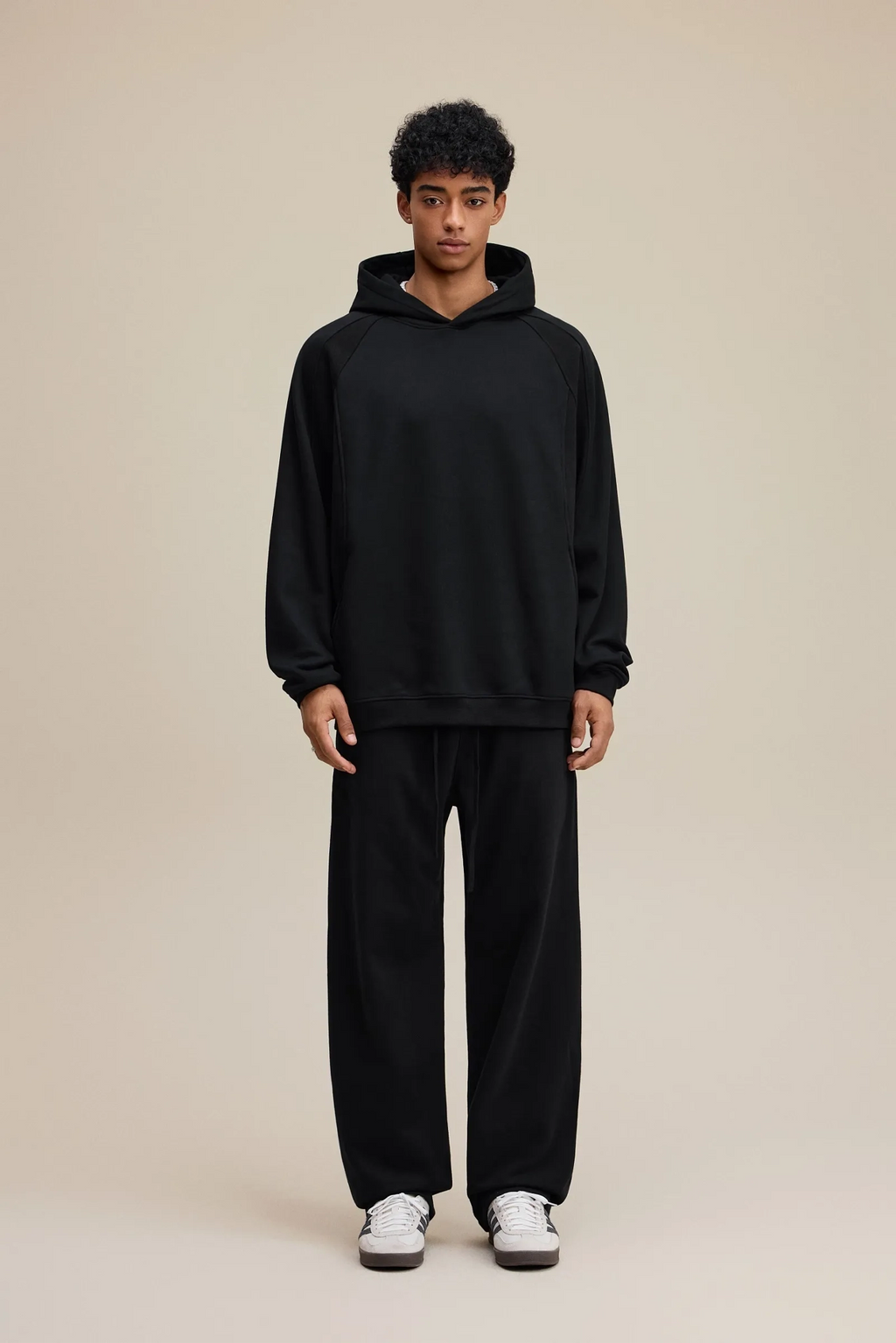 Person wearing a black hoodie and black pants on a beige background