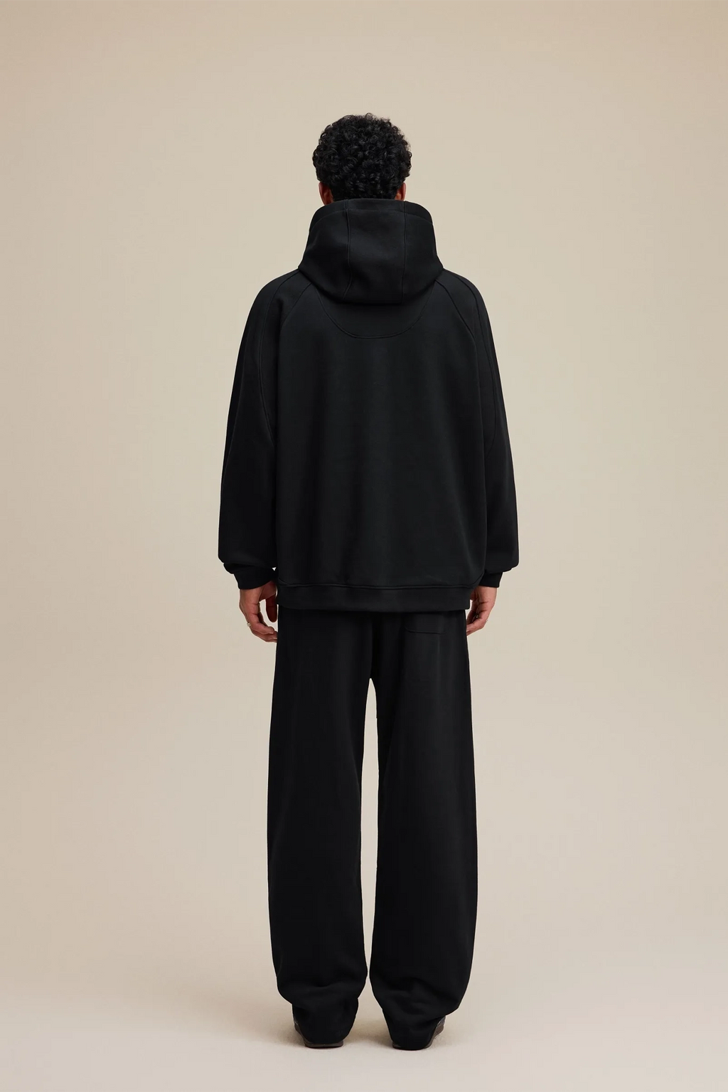Person wearing a black hoodie and pants on a beige background