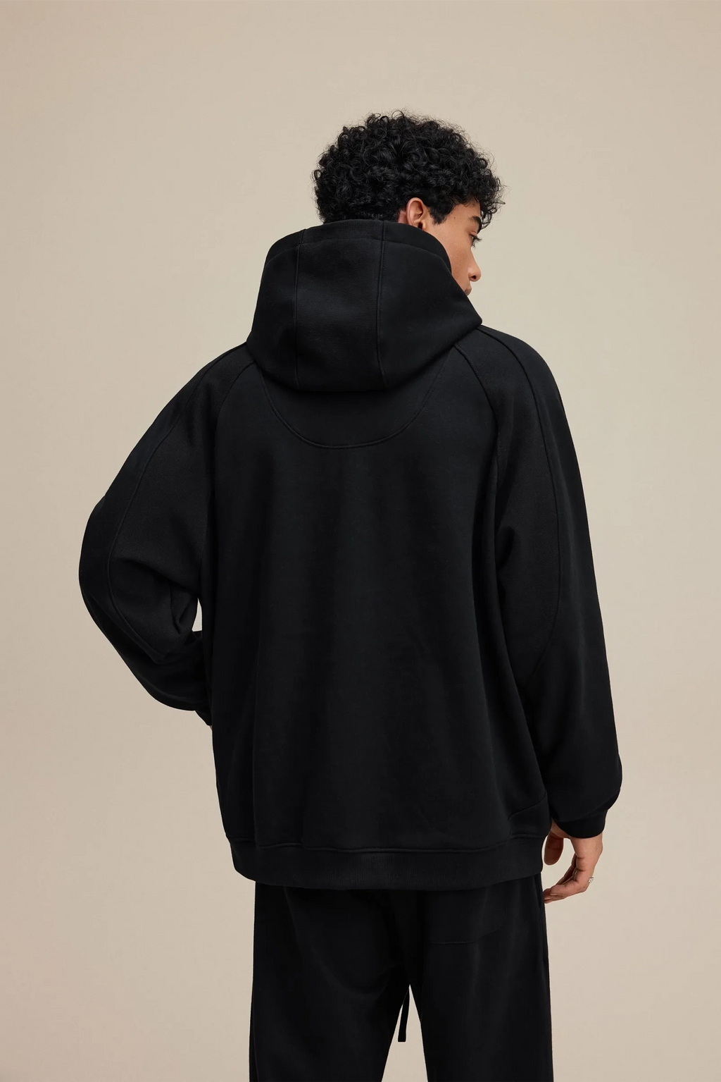 Person wearing a black hoodie from behind on a beige background