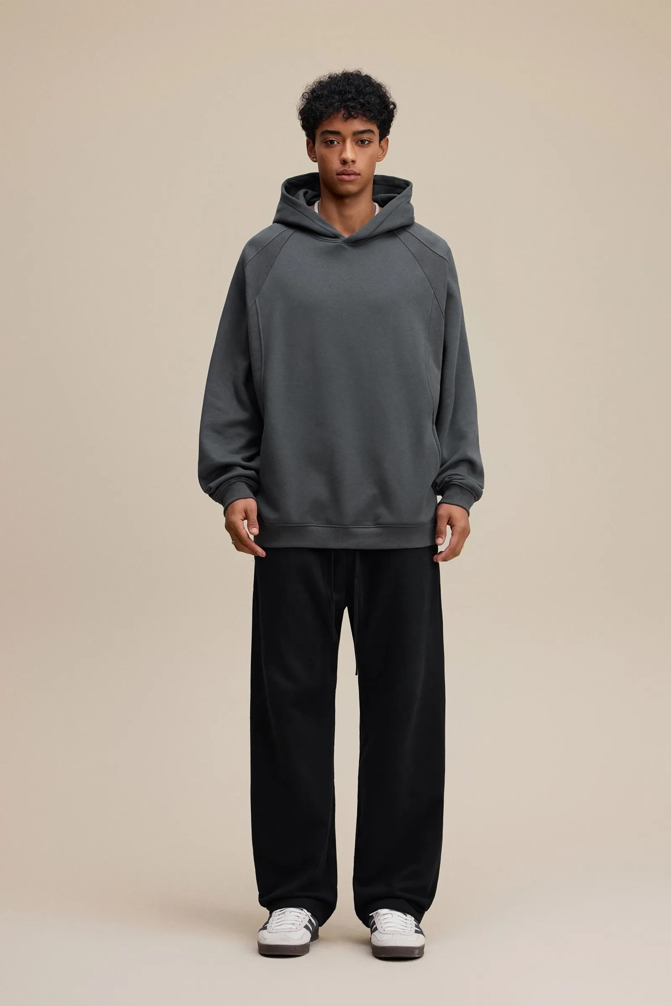 Person wearing a gray hoodie and black pants on a beige background