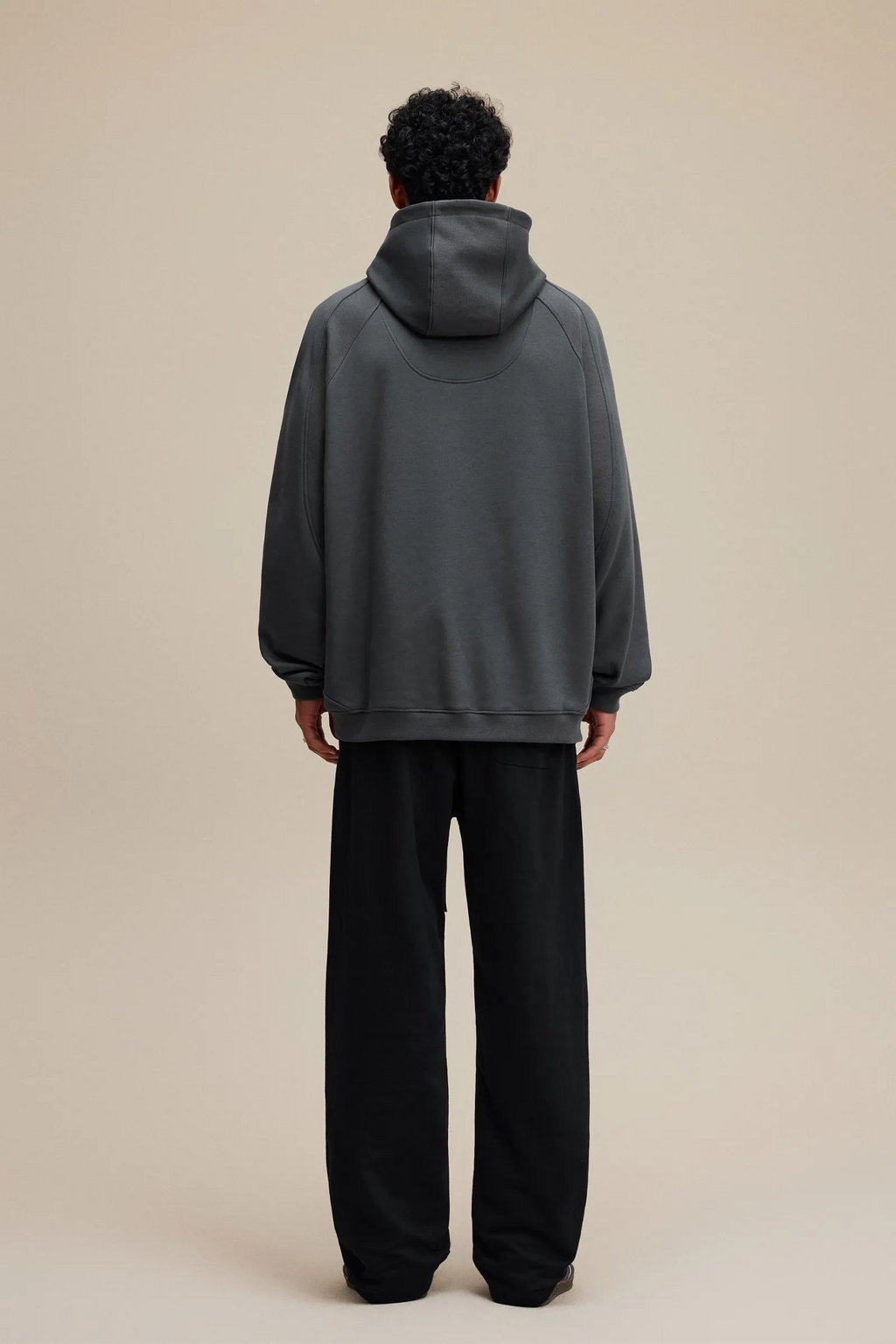 Person wearing a gray hoodie and black pants on a beige background