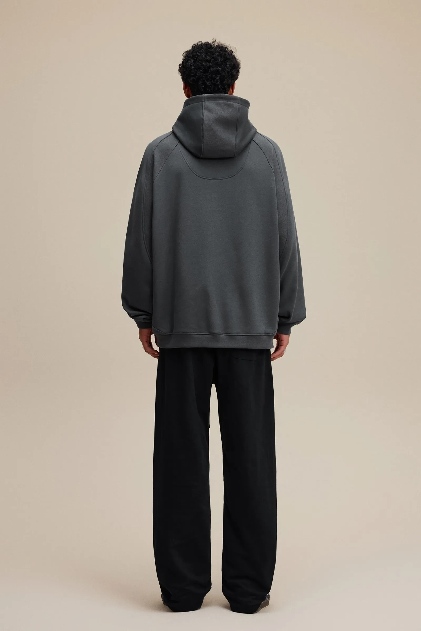 Person wearing a gray hoodie and black pants on a beige background