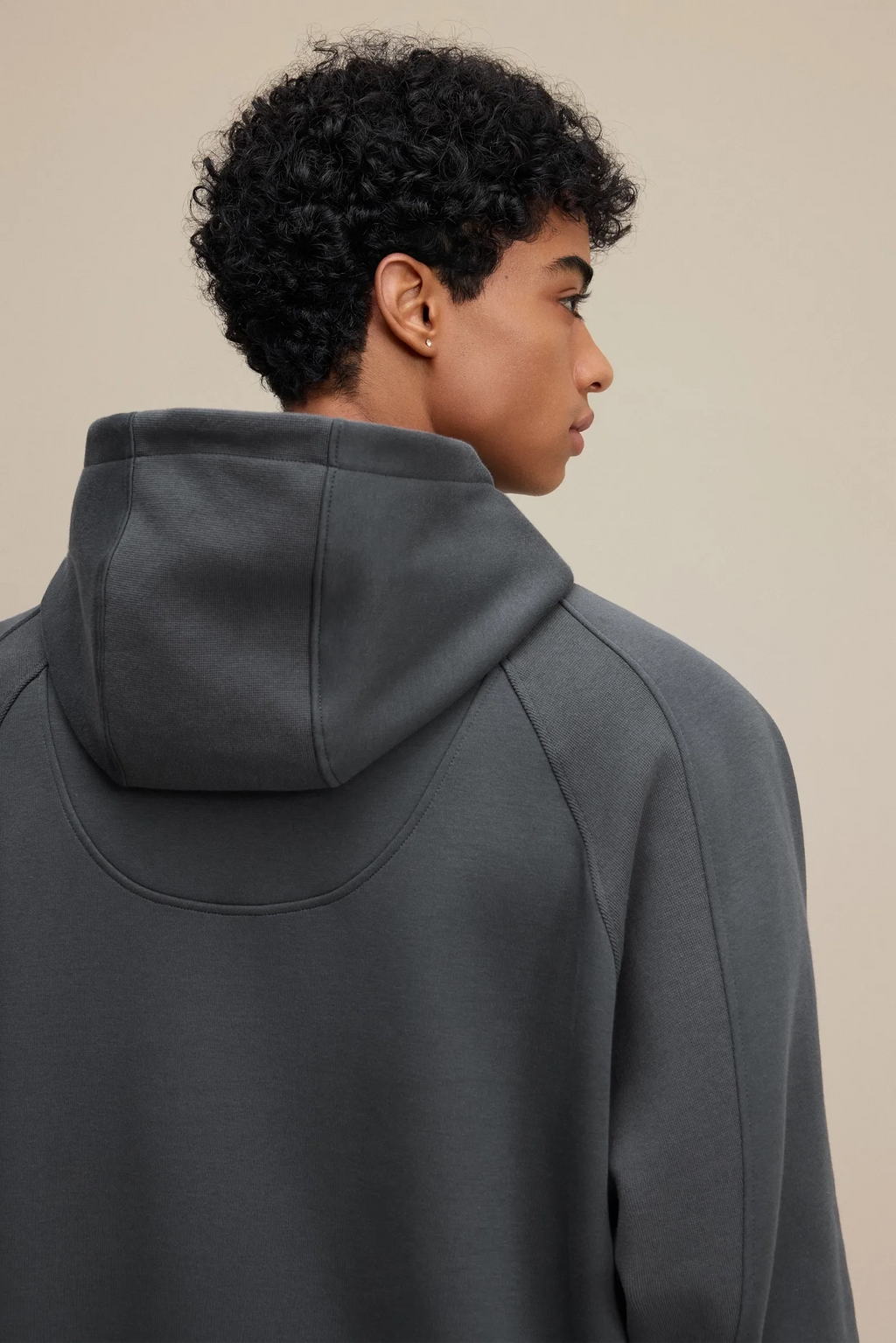 Person wearing a dark gray hoodie against a beige background