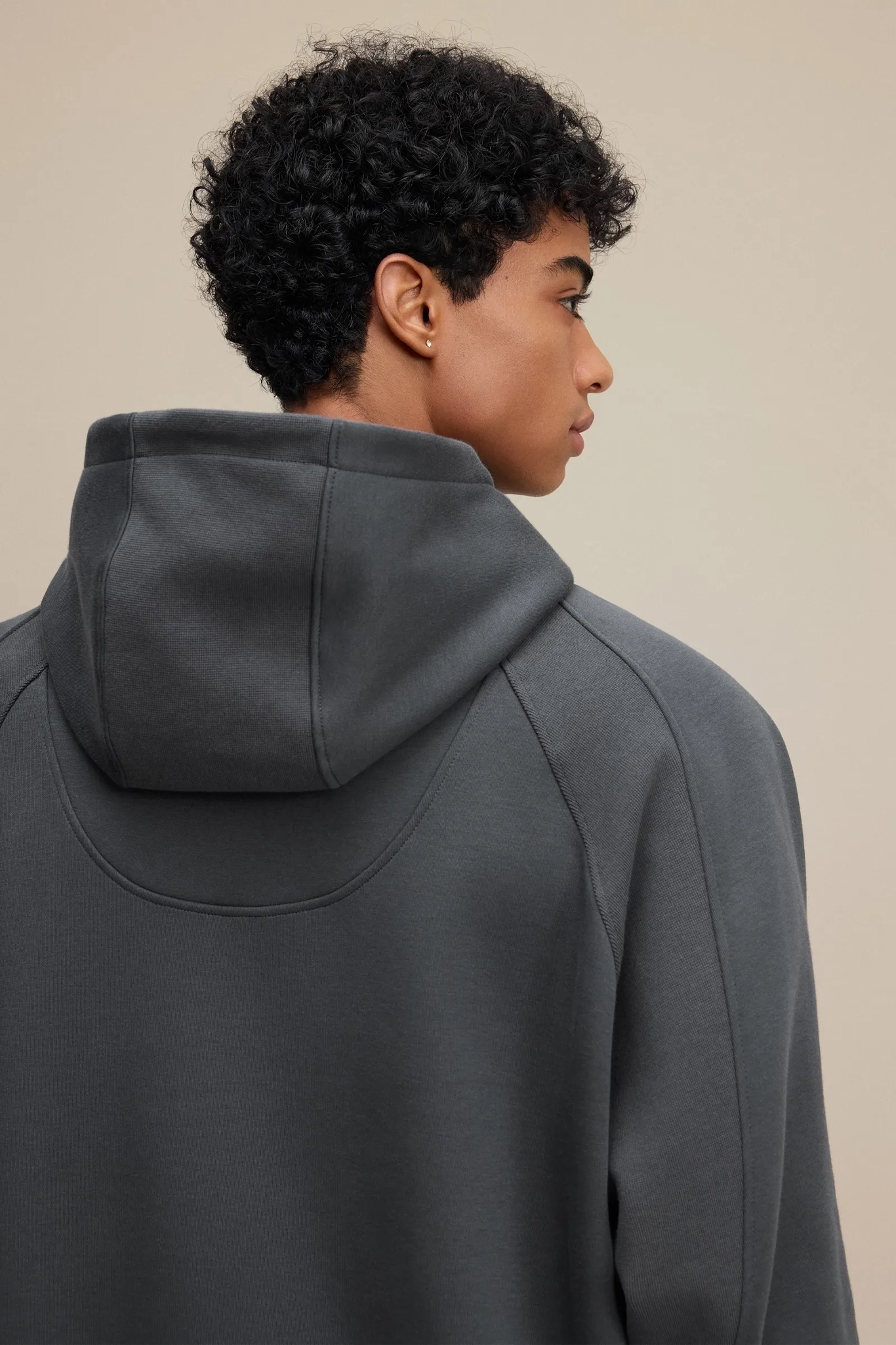 Person wearing a dark gray hoodie against a beige background