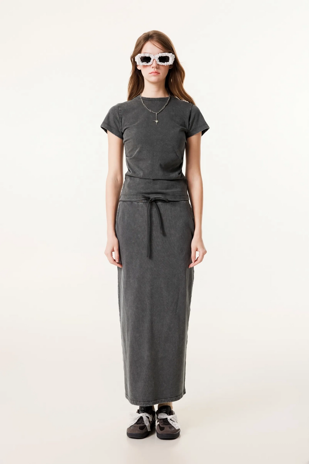 Person wearing a dark gray t-shirt and long skirt with sunglasses on a white background