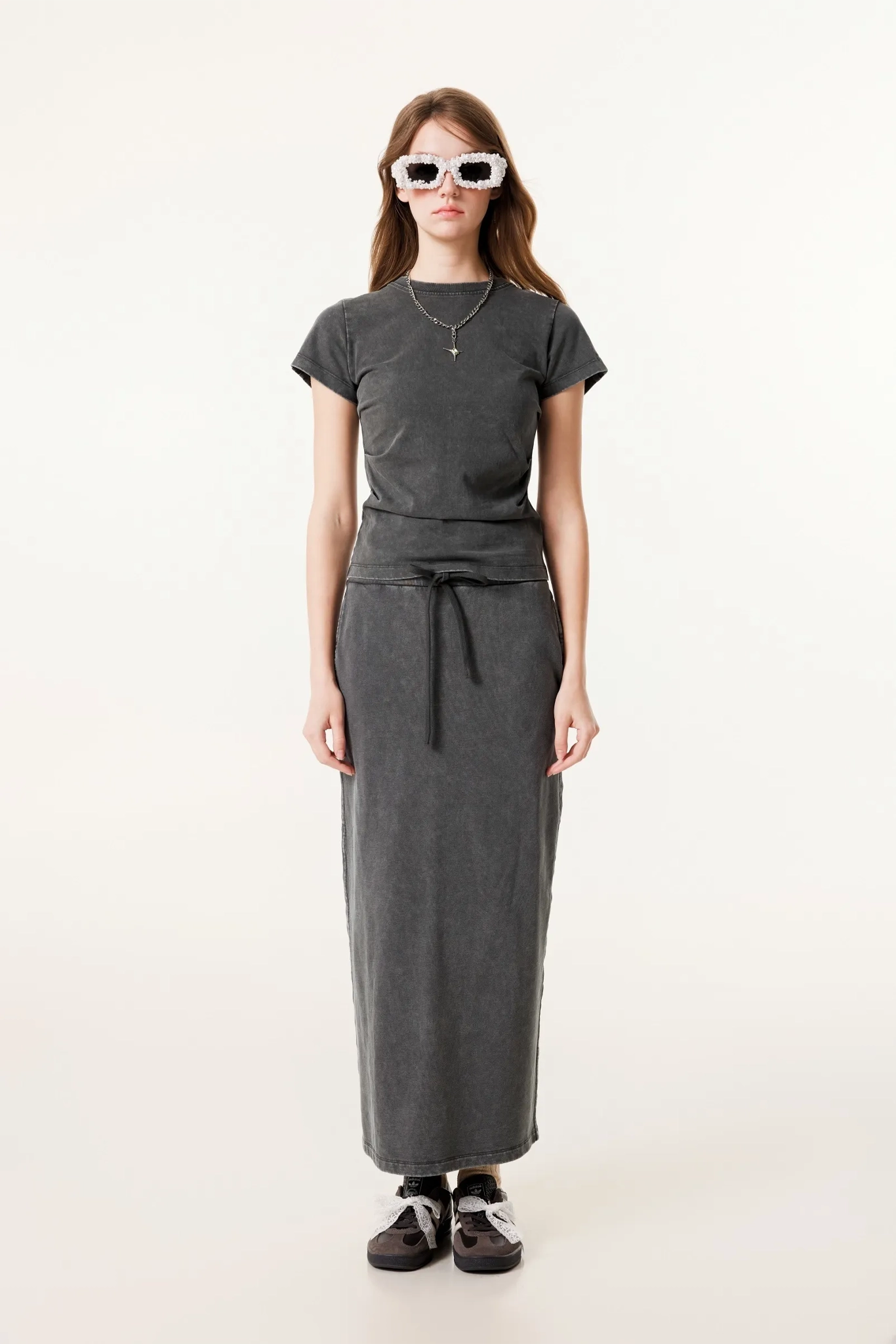 Person wearing a dark gray t-shirt and long skirt with sunglasses on a white background