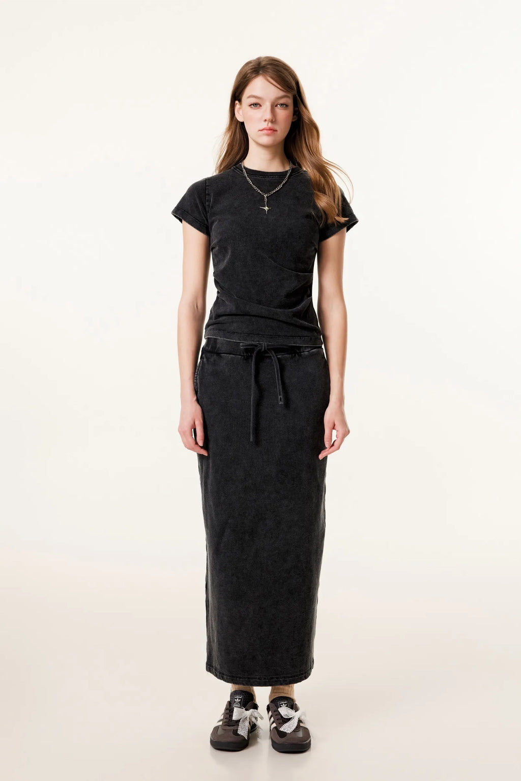 Person wearing a black t-shirt and long black skirt on a white background