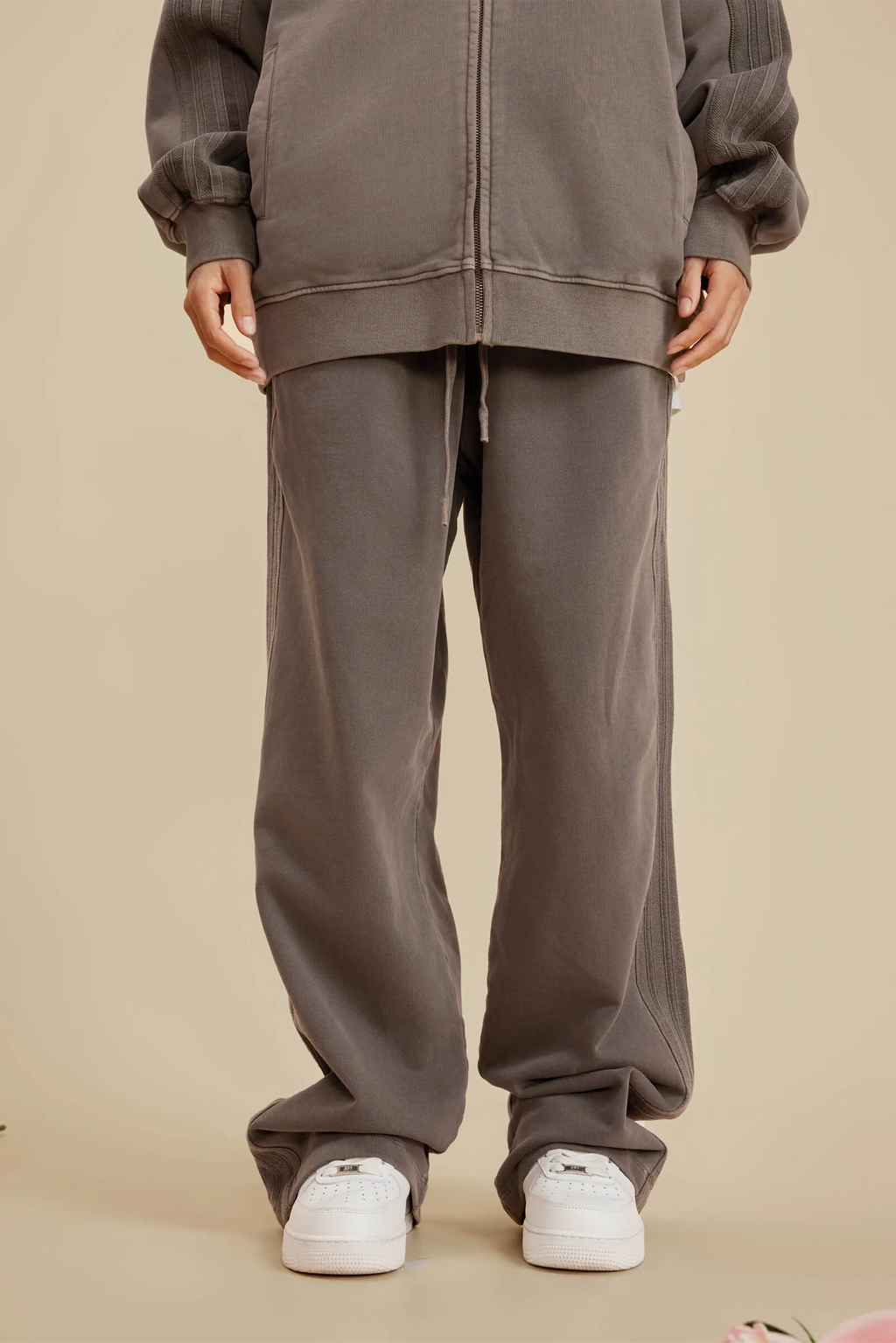Person wearing a gray tracksuit with white sneakers on a beige background