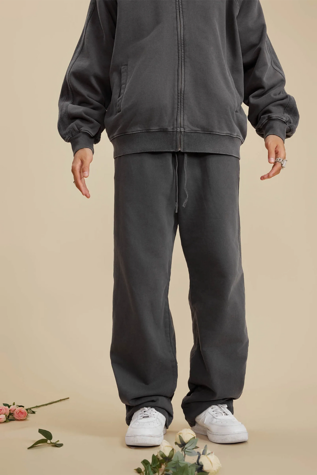 Person wearing a dark gray tracksuit with white sneakers on a beige background