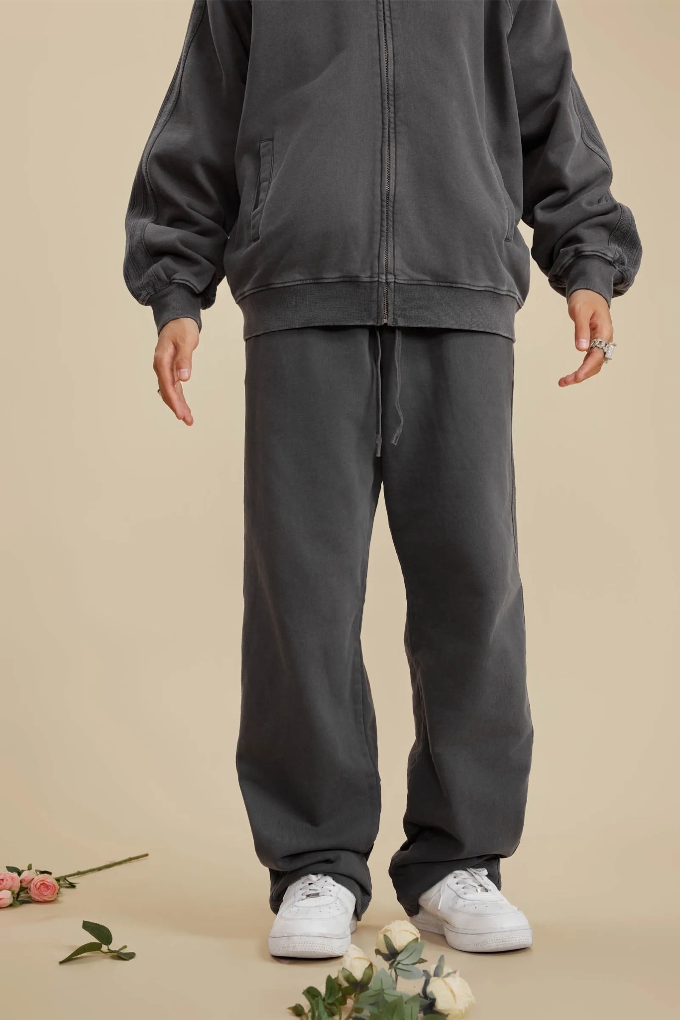 Person wearing a dark gray tracksuit with white sneakers on a beige background