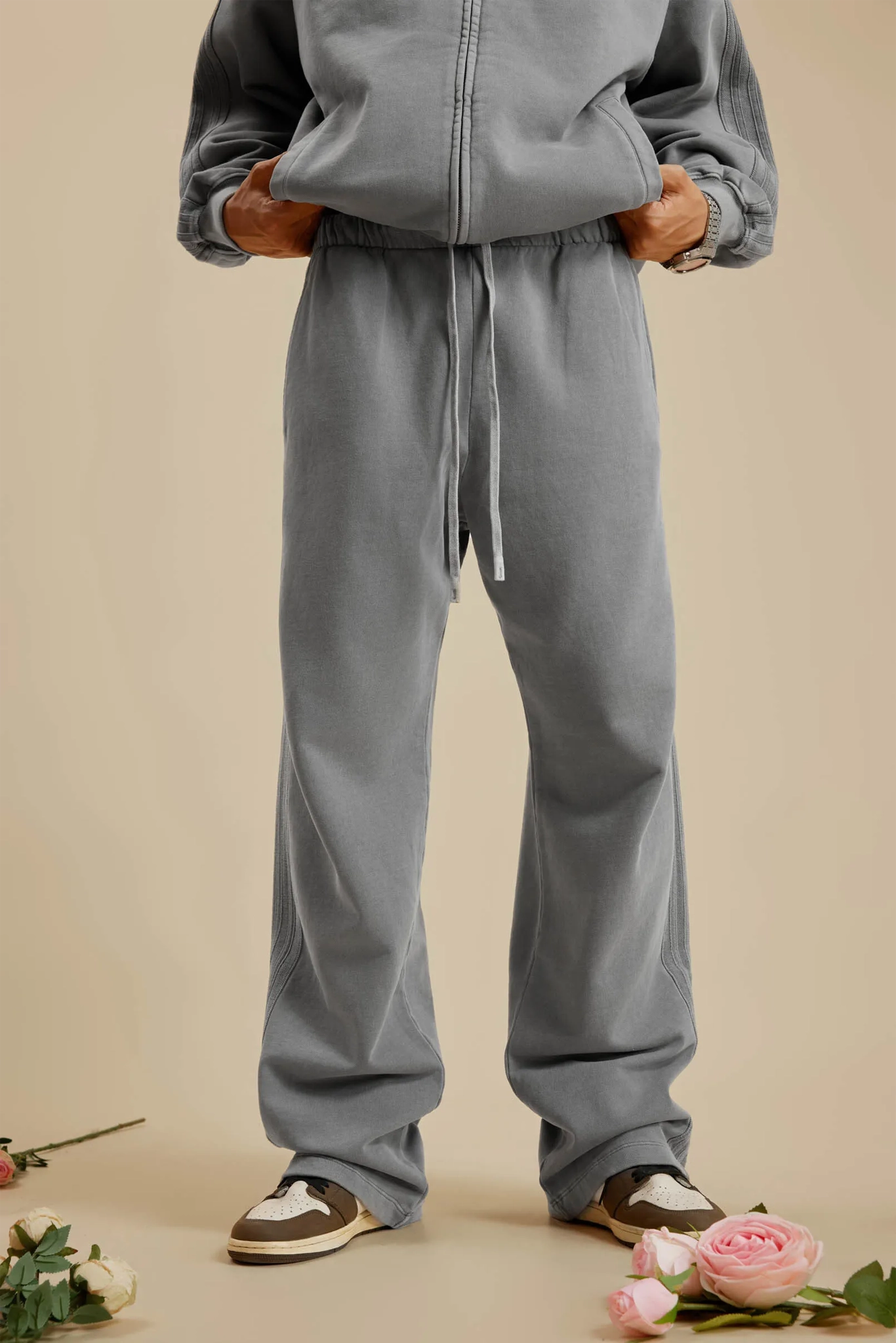 Person wearing a gray tracksuit with floral decorations on a beige background