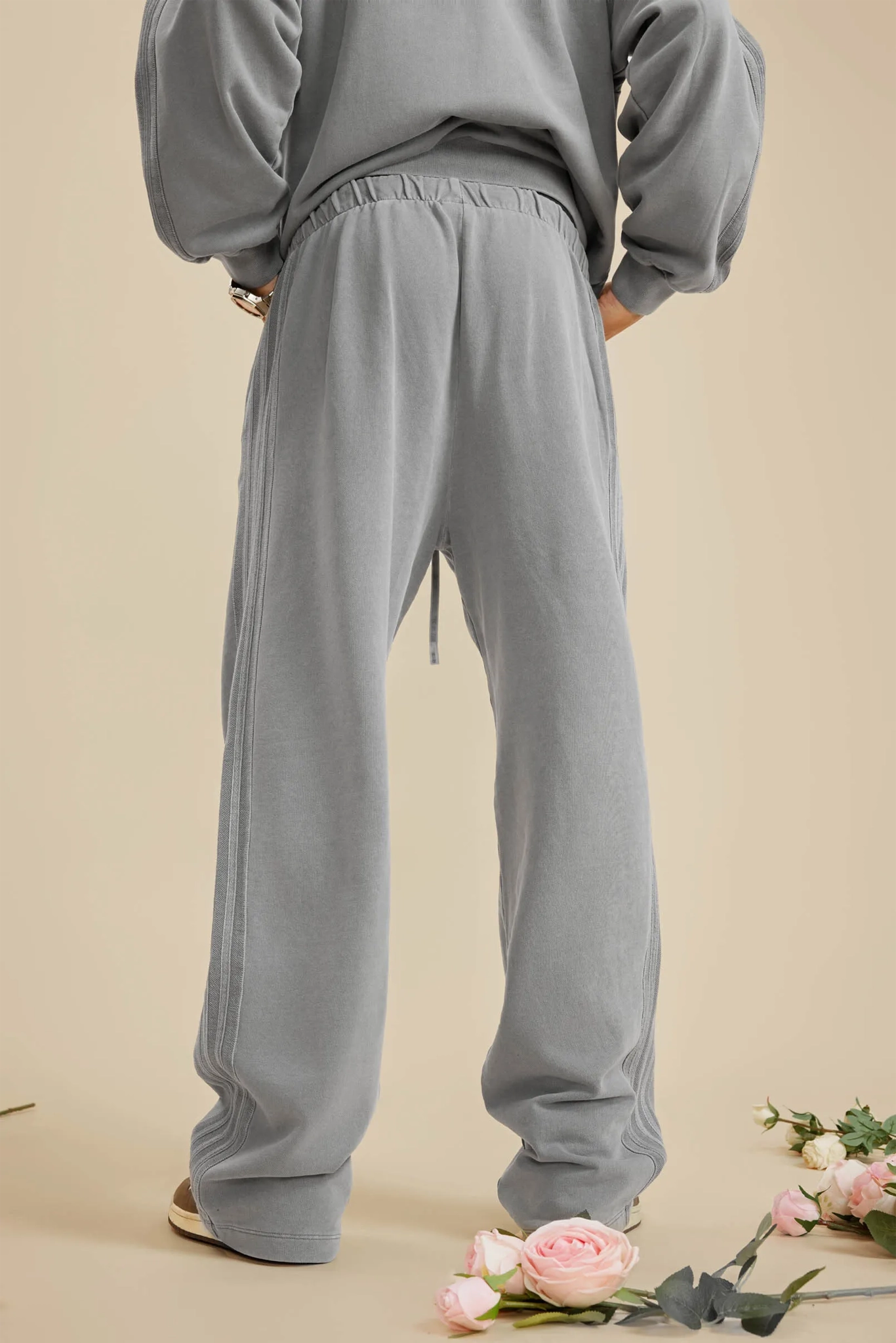 Person wearing gray sweatpants on a beige background with flowers at the bottom.