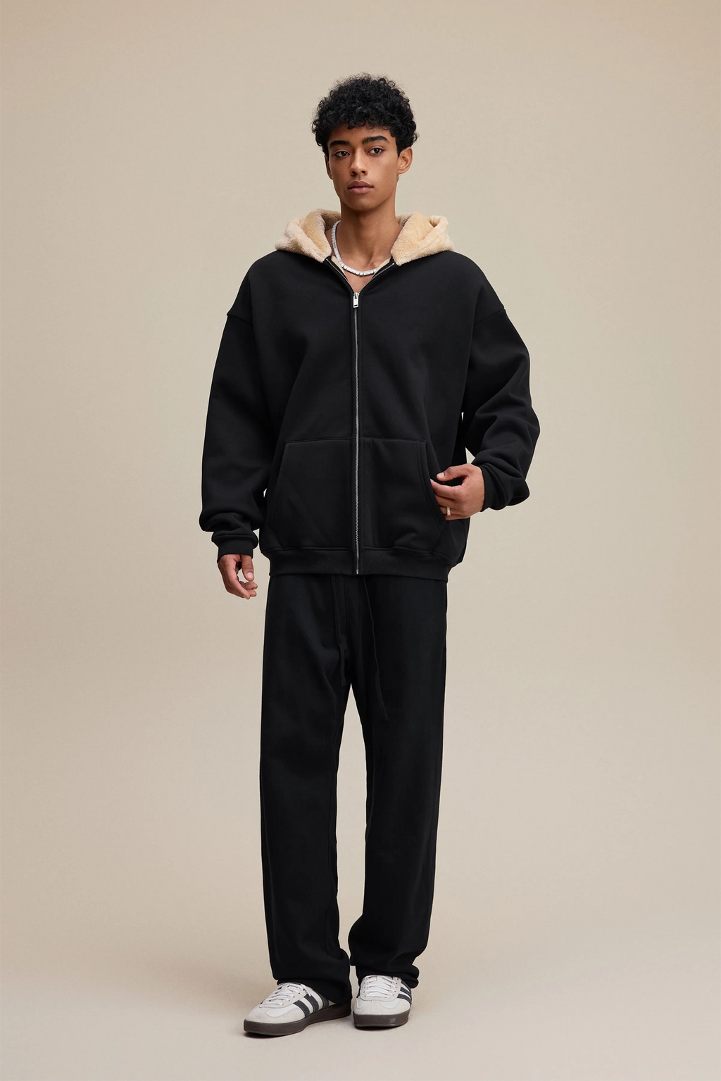 Person wearing a black hoodie with beige lining and matching pants on a beige background