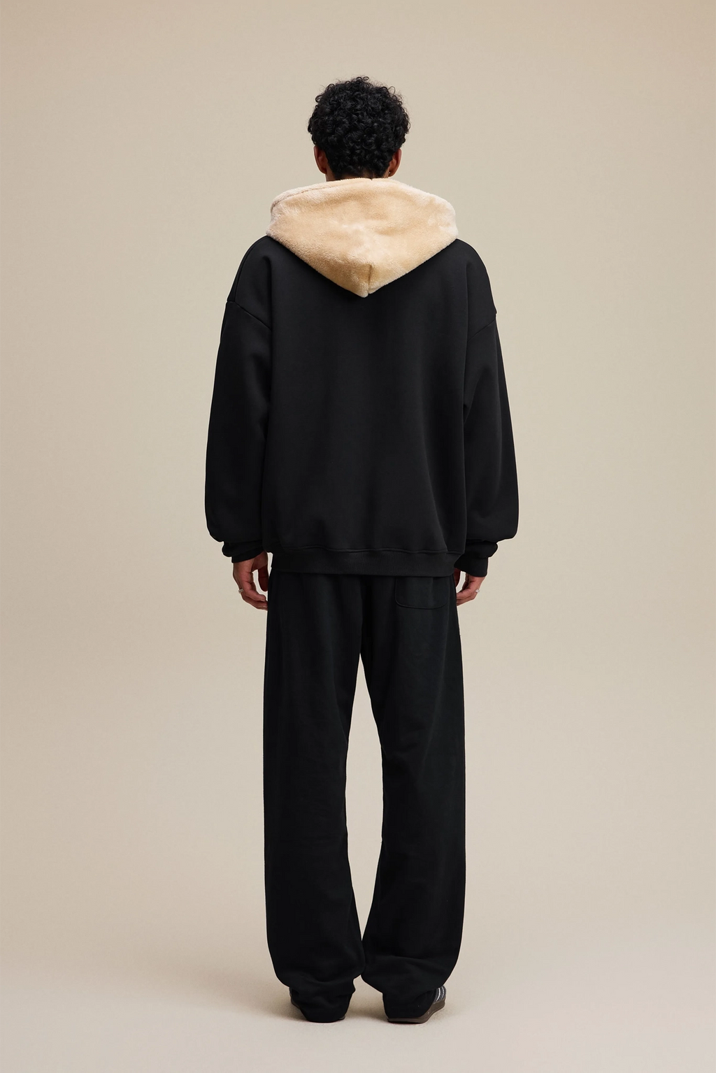 Person wearing a black hoodie with beige hood on a beige background