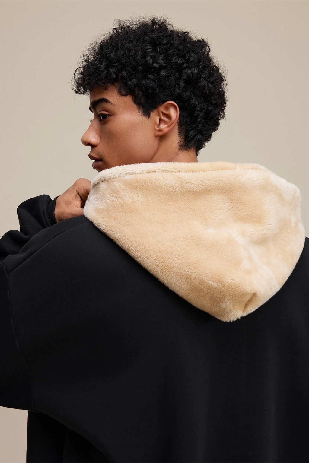 Person wearing a black coat with beige fur lining on a beige background
