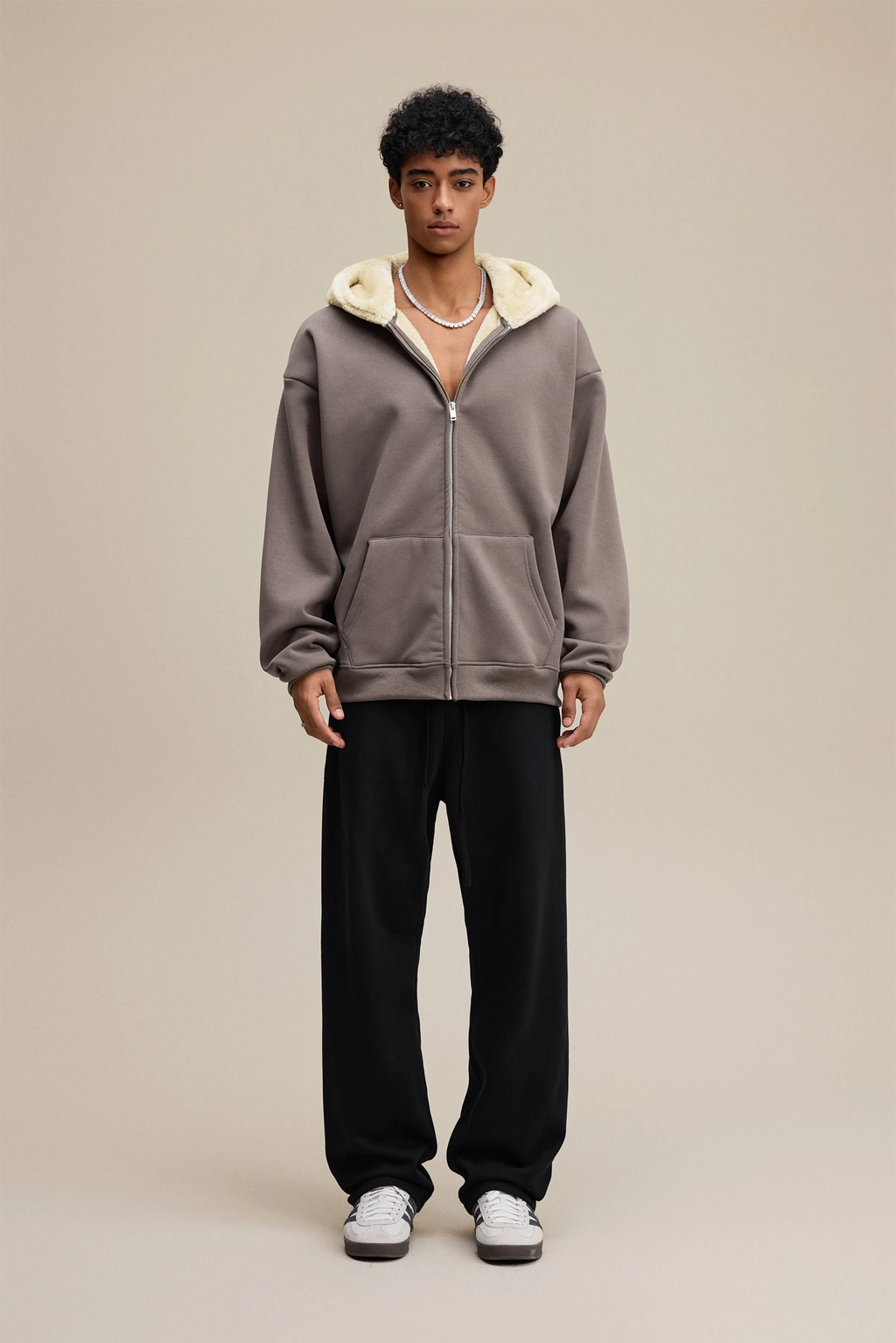 Person wearing a gray hoodie with a white hood and black pants on a beige background