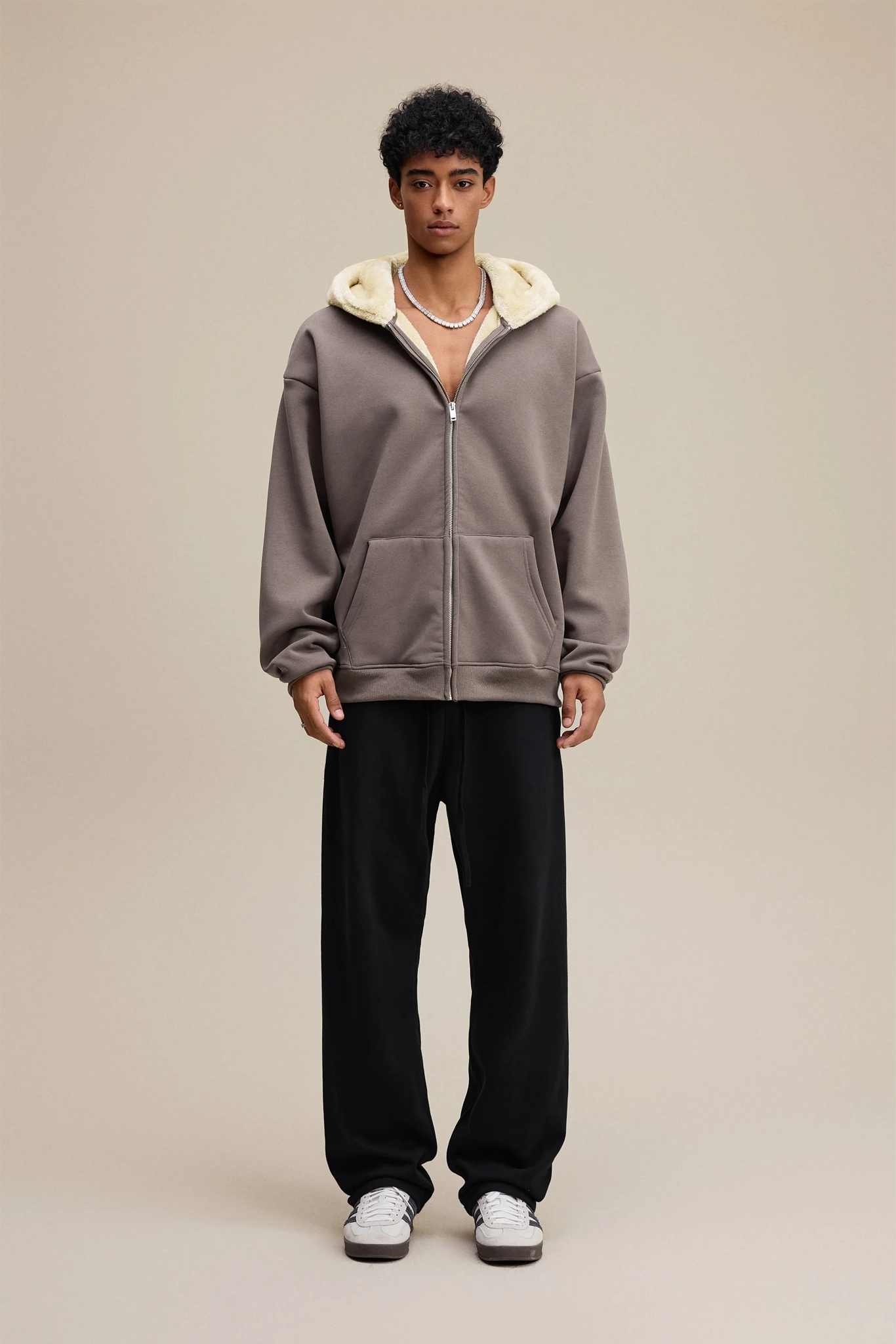 Person wearing a gray hoodie with a white hood and black pants on a beige background